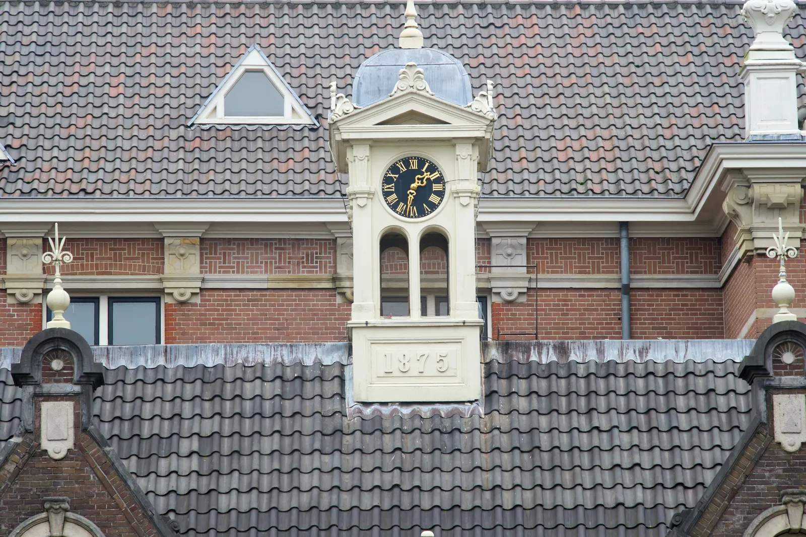 A little tower surrounded by roofs. The year 1875 is shown at its base. It has some ornaments, and a few small arches. It also has a clock that points at 32 minutes past one.