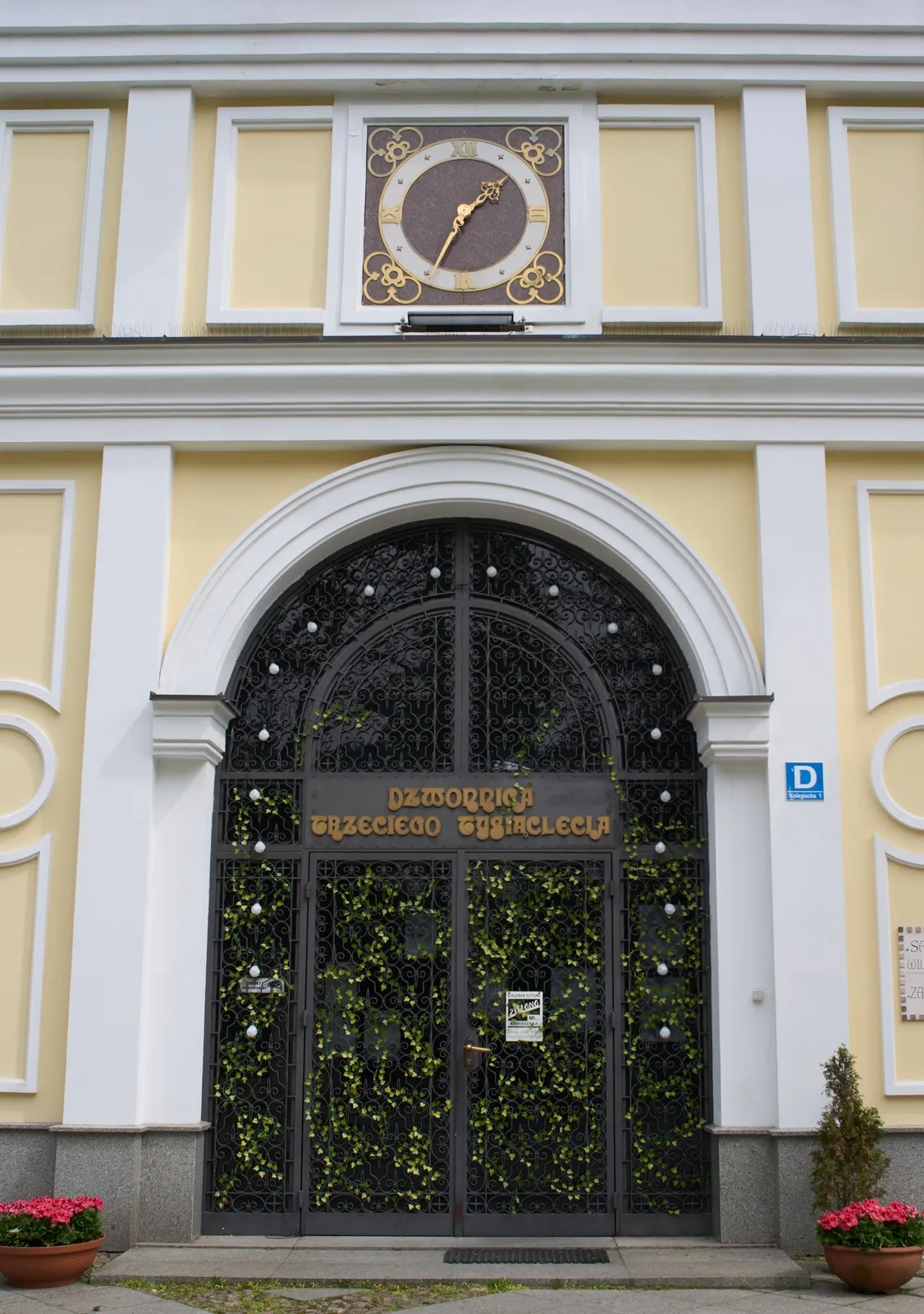 A clock on an old, yellow gate to what seems to be a garden. It points at 26 minutes to 2.