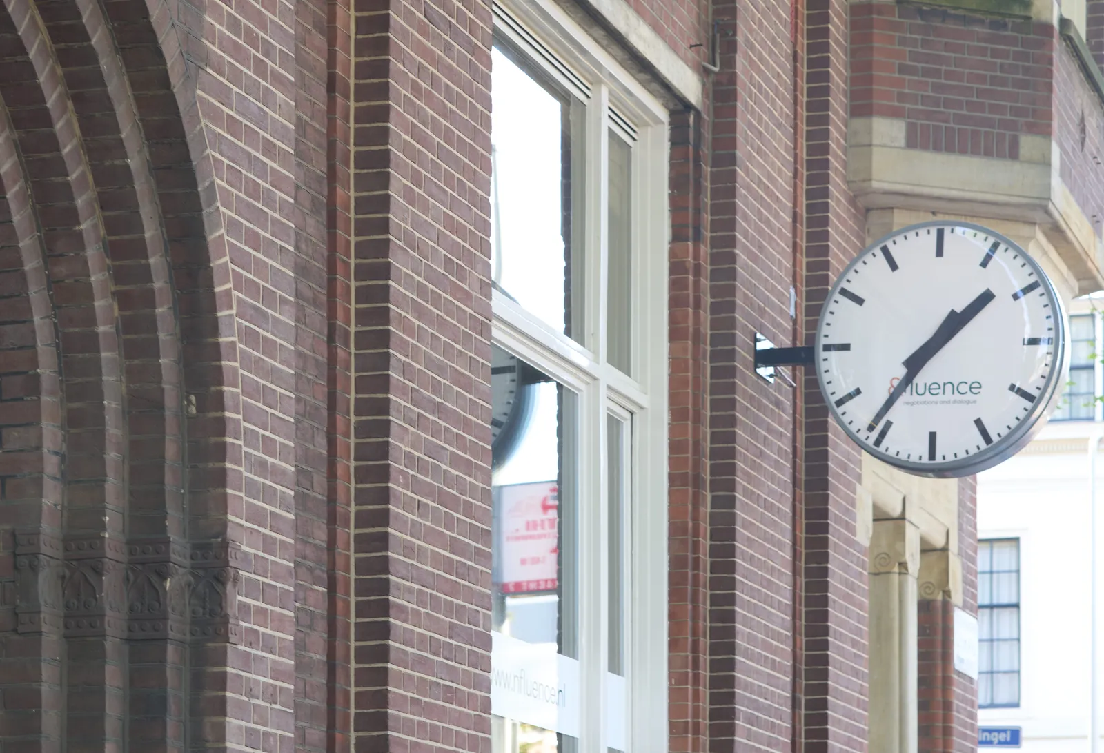A brick building with part of an arc visible. Attached to this building there’s a clock. It points at 36 minutes past one.