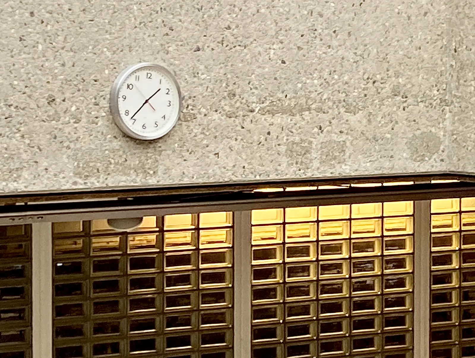 On a wall above some green windows there’s a clock. It points at 37 minutes past one.