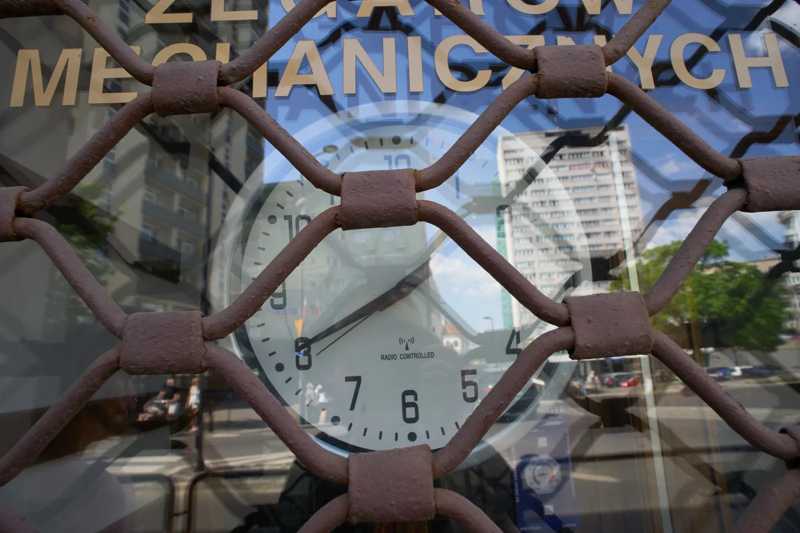 A clock in a shop window. The roller shutter is down, but you can still see that the clock points at 20 minutes to 2.