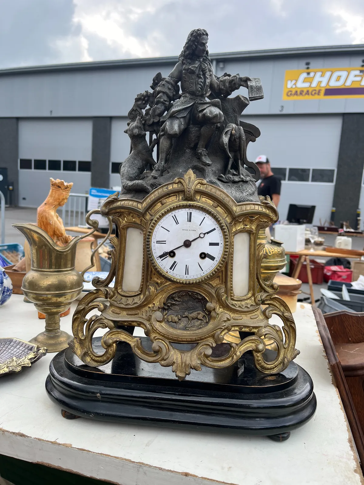 A richly ornamented clock for sale on this thrift sale. There are leave like ornaments surrounding the clock, and there’s a small relief of a fox and a sheep. On top of the clock there’s a statue of a wise person, probably a humanist, with a fox and a heron on his sides. The clock is a bit off, but let’s just assume that it points at 20 minutes to 2.  