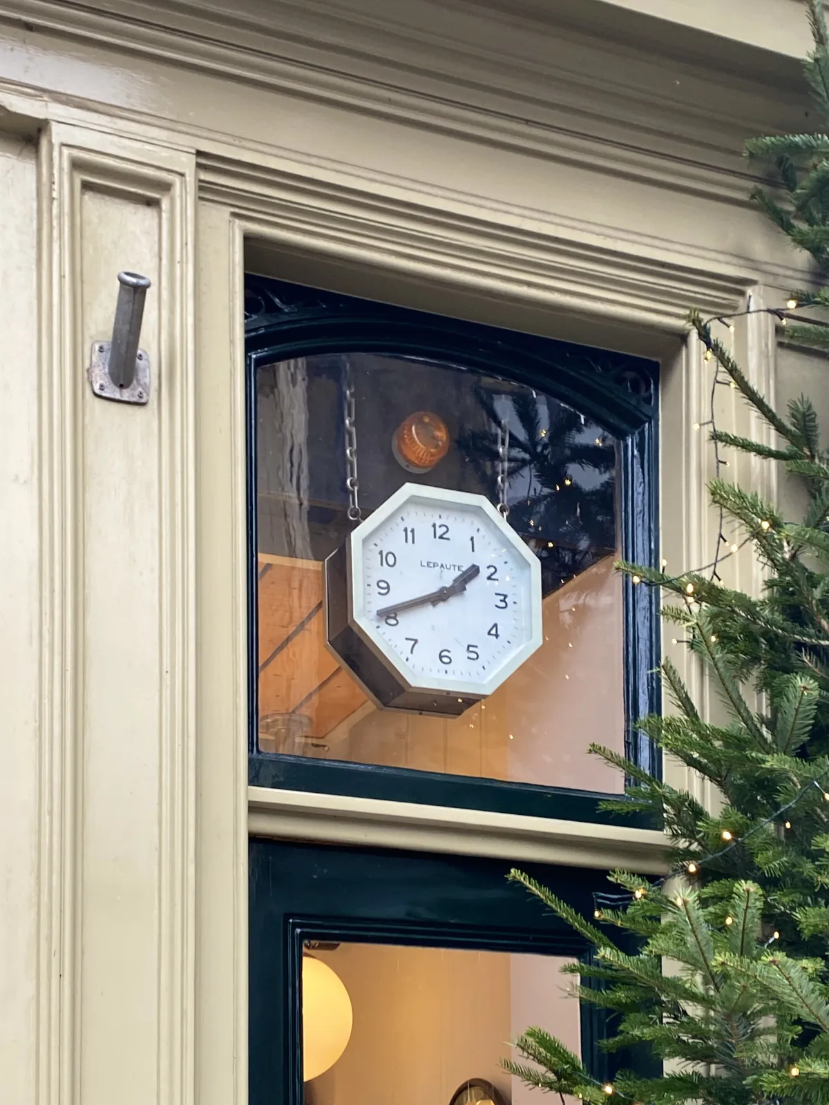 A clock in the shape of an octogon, hanging from metal chains behind a window. It points at 19 minutes to 2.