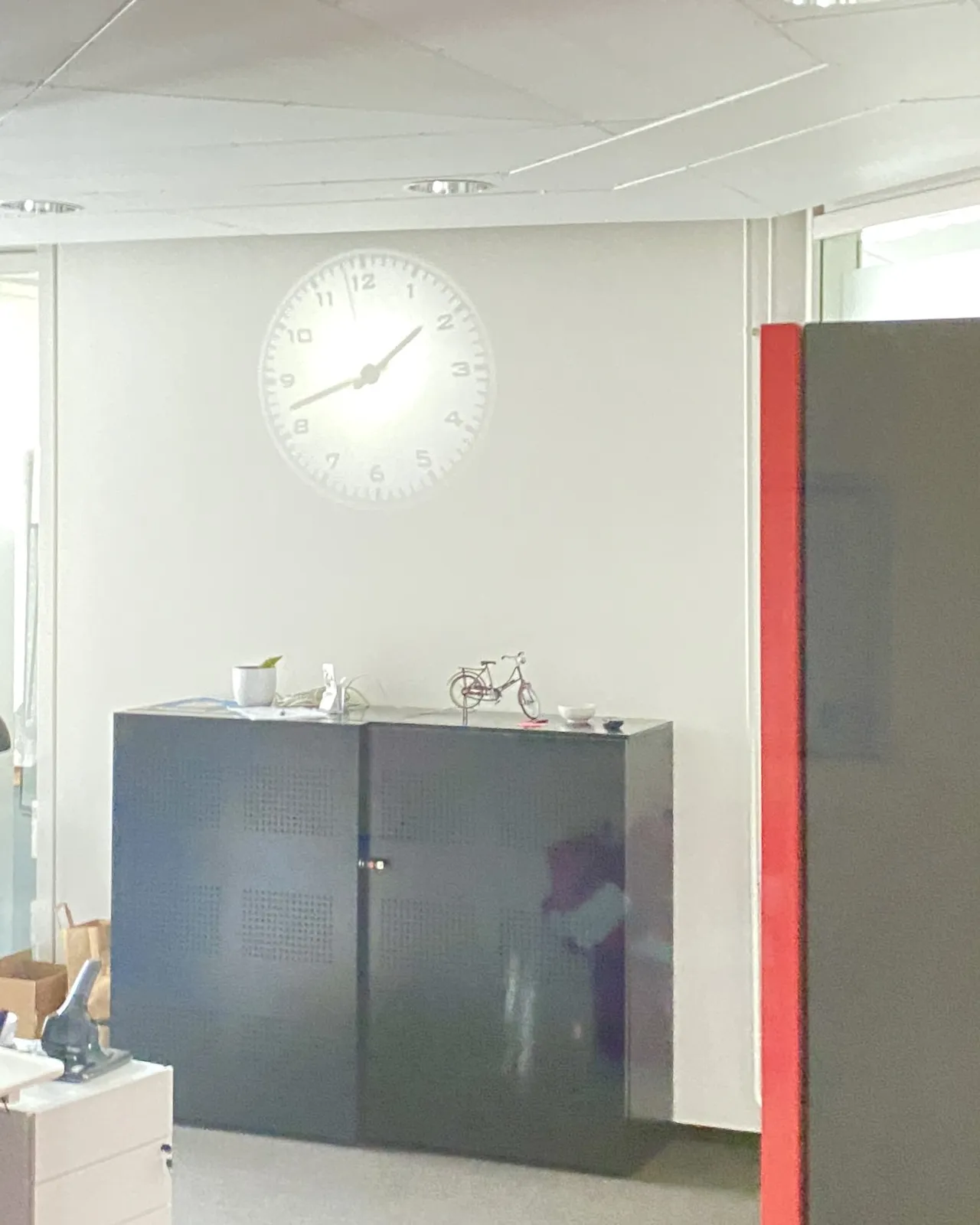 A projection of a clock on a wall in an office. The clock points at 18 minutes to 2.
