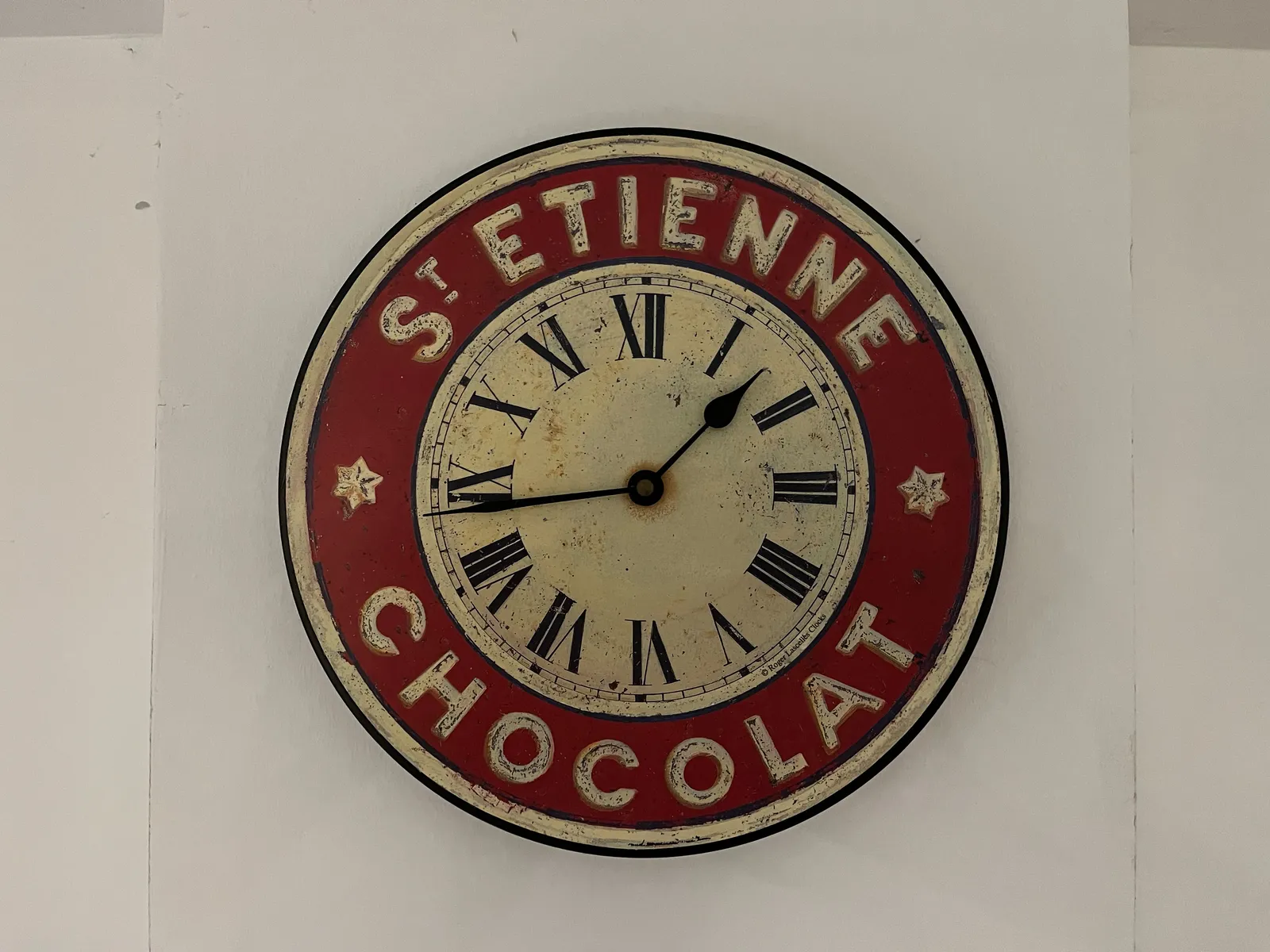 A clock, it looks a bit worn, with the words St Etienne Chocolat on it. On the clock it is 17 minutes to two.
