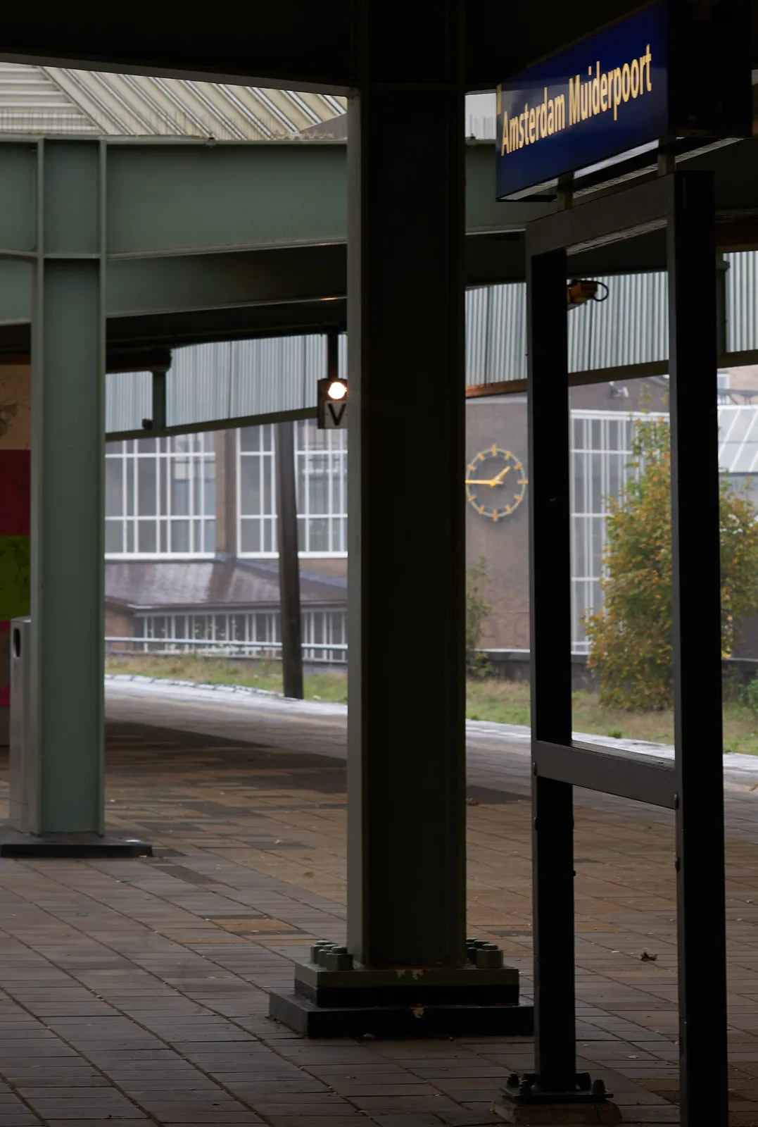 Standing on a platform on train station Amsterdam Muiderpoort, peeking thought a few columns. There’s a clock in the distance that points at a quarter to two.