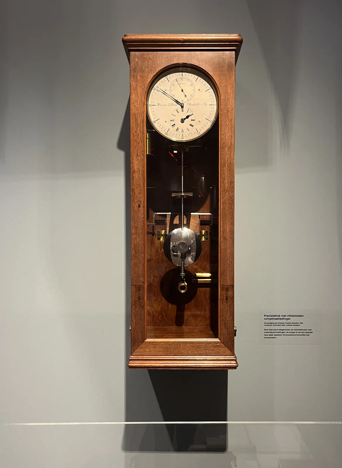Next to this old wooden clock there’s a sign in Dutch that says that this is a precision clock with a pendulum made from nickel. It has three separate dials. The small one at the top displays the seconds and points at 55. The small one at the bottom shows the hours, and points at almost two. And the main dial shows the minutes, and this one points at 51.