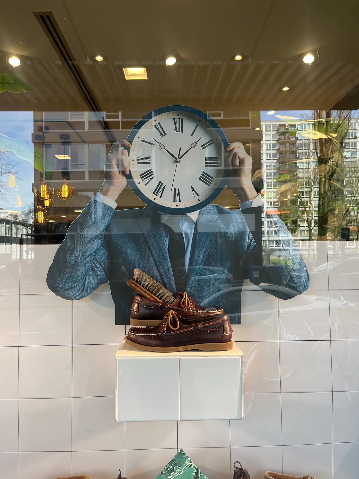 In a shopping window of a shoe shop stands this cutout billboard of a person in a suit holding a clock in front it their head. Both hands of this clock are the same size, so it’s either 8 minutes to two, or 7 minutes past ten.