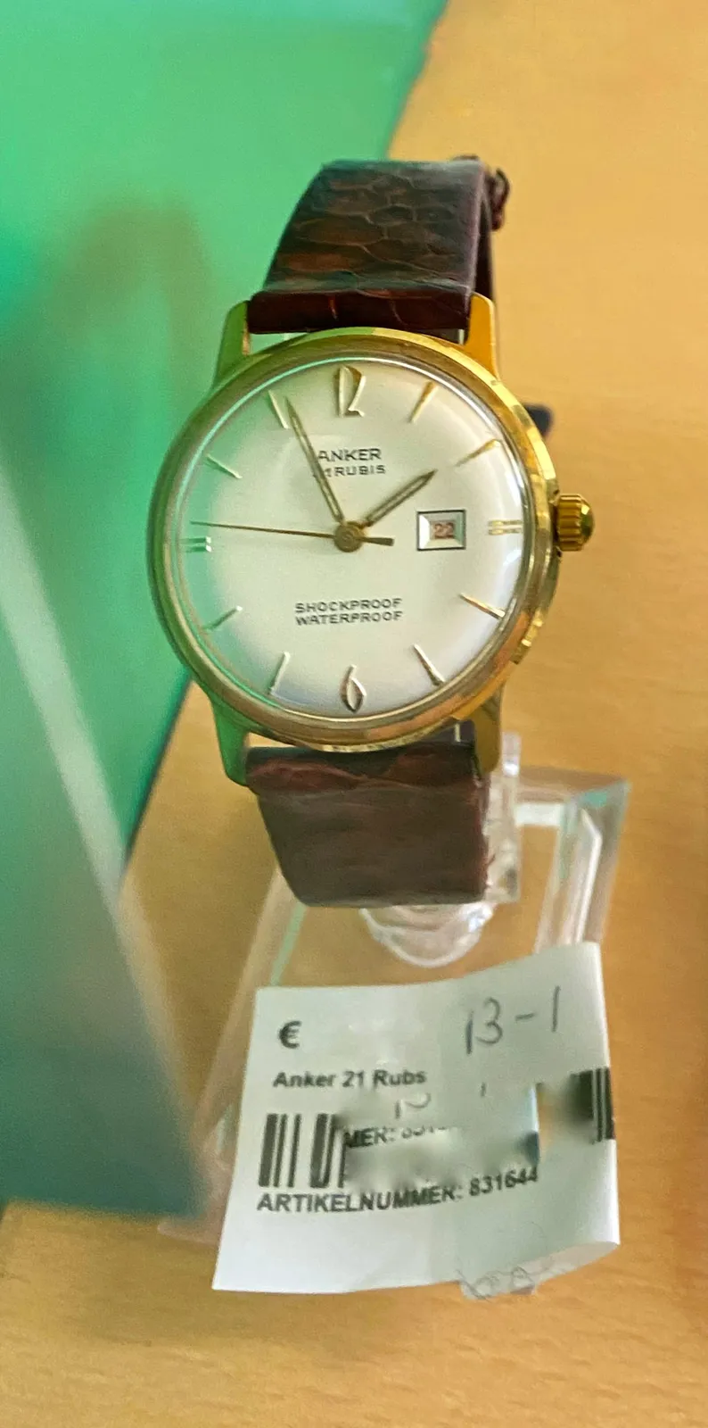 A simple wrist watch, it says it is both shockproof and waterproof. The name of the maker is probably incomplete since one of the hands covers its first letter: anker rubis is readable.  The watch points at 4 minutes to 2.