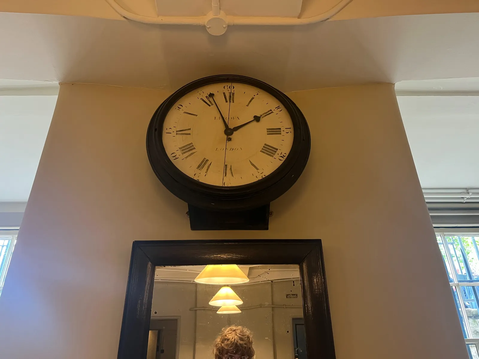 The top of the head of the photographer is visible in an old mirror. Above the mirror there’s an old clock that points at 4 minutes to 2.