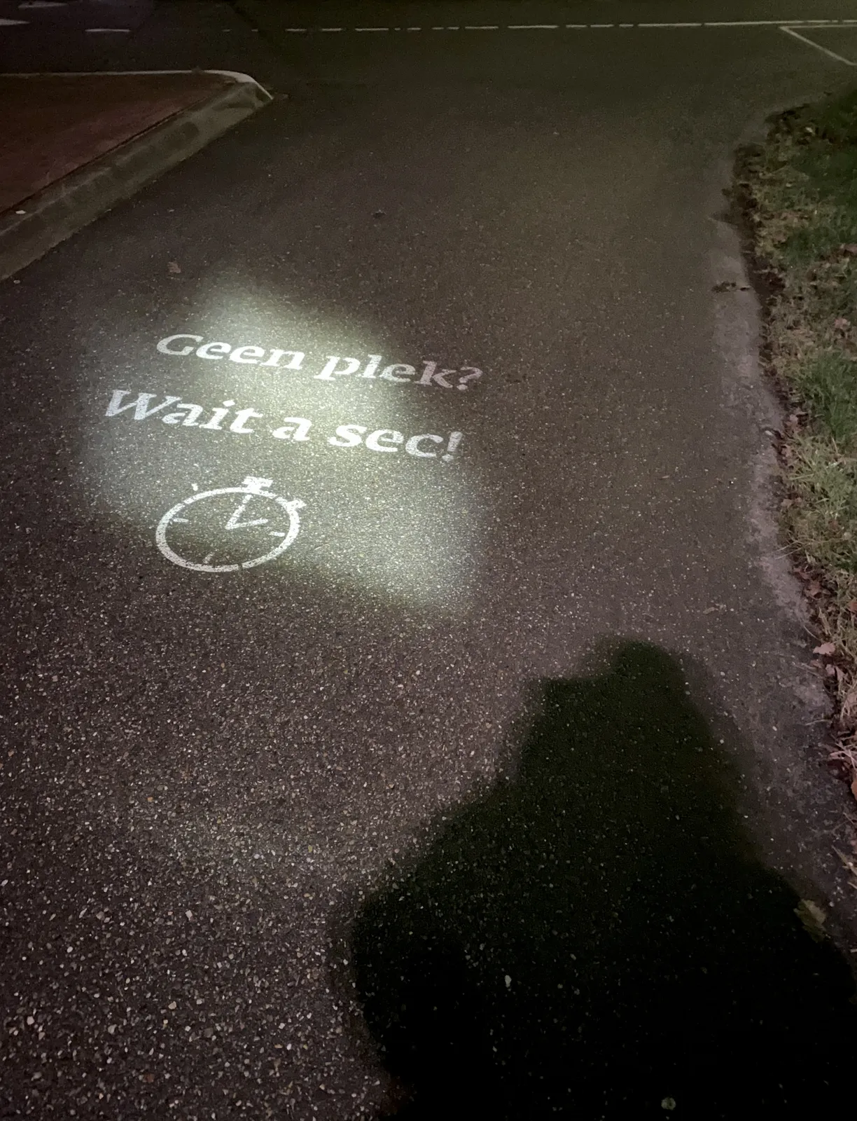 On the asphalt a half Dutch, half English slogan is printed: geen plek wait a sec (which translates to No Place, wait a sec). A clock is printed below it. It points at two o’clock.