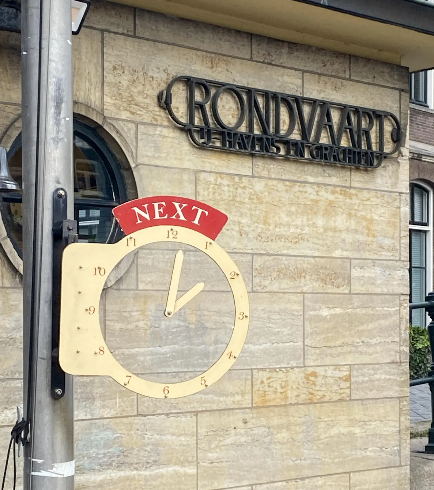 A clock in front of a building with a cast iron advertisement for boat trips through the harbour and the canals. The hands of the clock seem to float in the air. They point at 2 minutes past 2.
