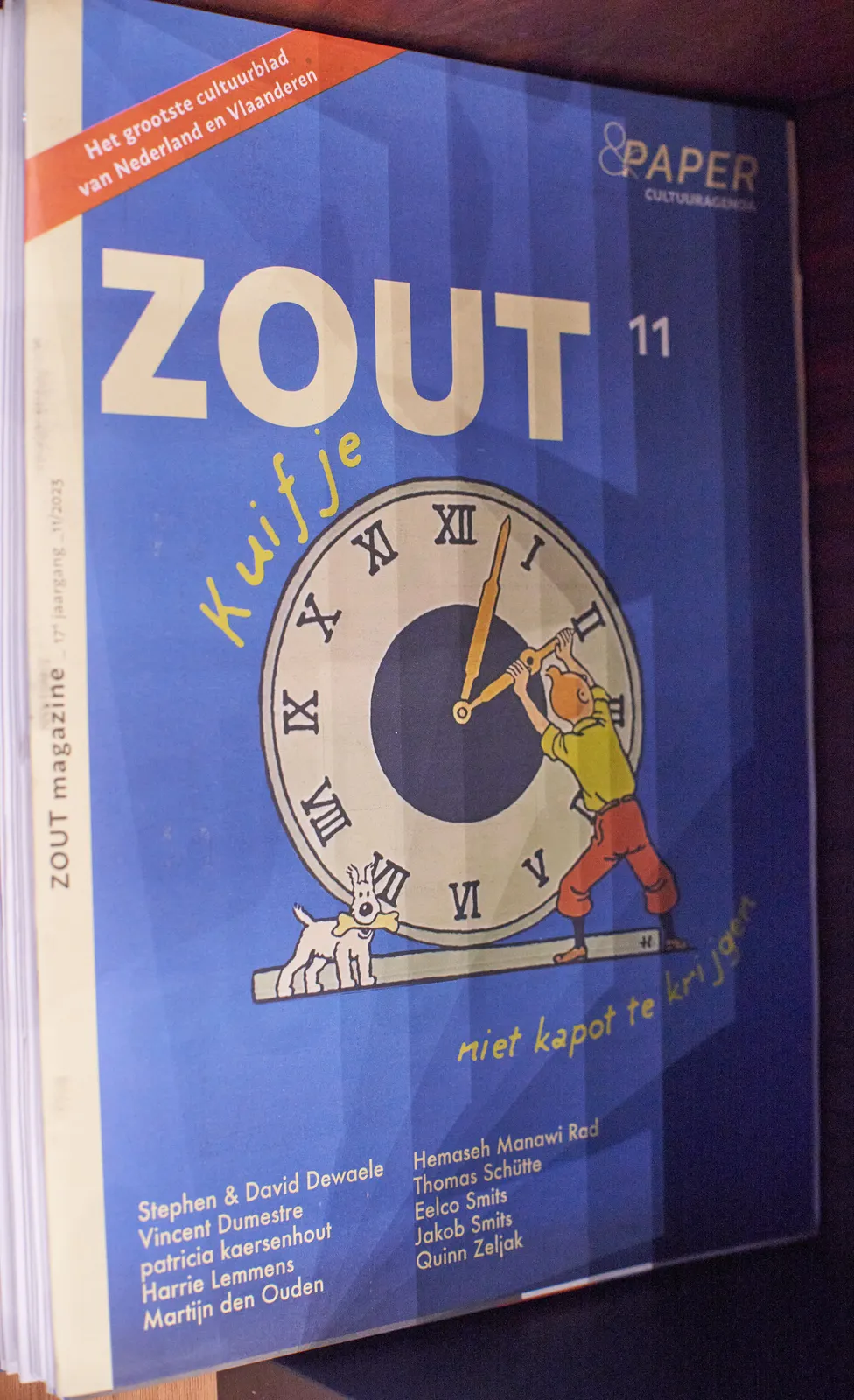 On the cover of a blue magazine about culture called Zout there’s a print of Tintin and his dog. Tintin is trying to move the hour hand of an enormous clock. The clock points at approximately 2 minutes past 2.