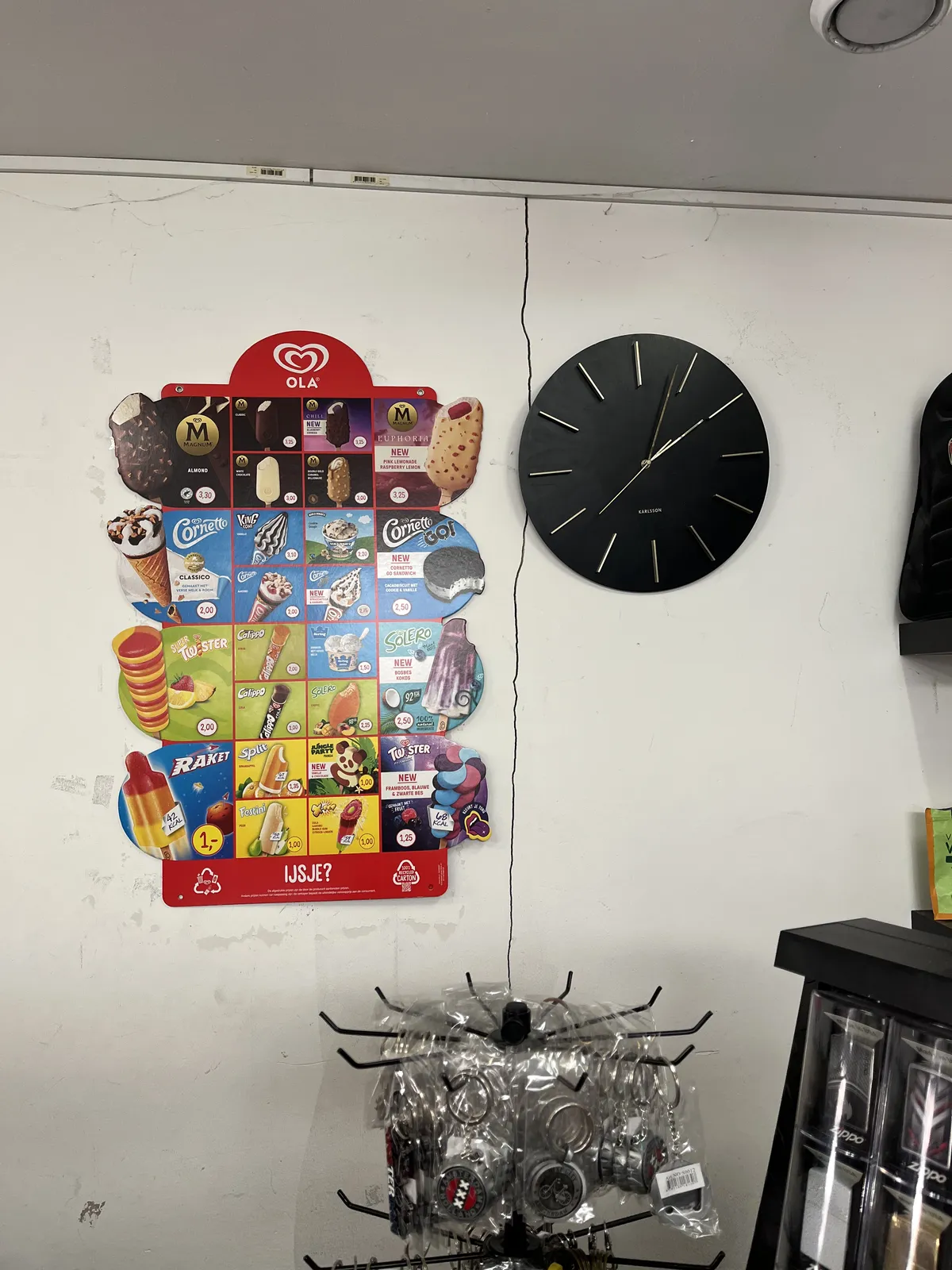 In a shop that seems to sell some touristy things and factory made ice cream, there’s a wall clock that seems to point at 3 minutes past two.