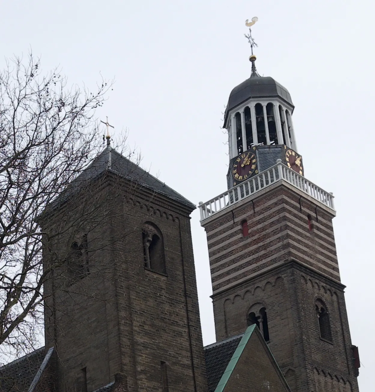 A clock on an old church tower. The tower has stripes and a little dome. The clock points at 5 past 2.