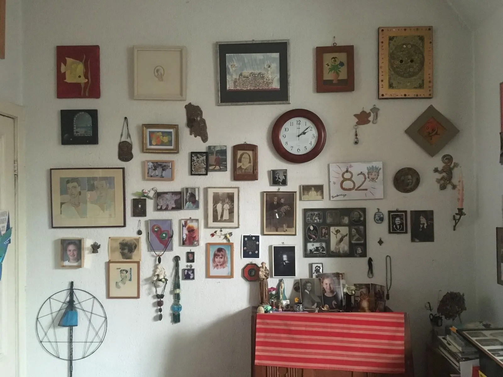 There are many photographs and works of art on this wall. There’s also a clock that says it’s eight minutes past two.