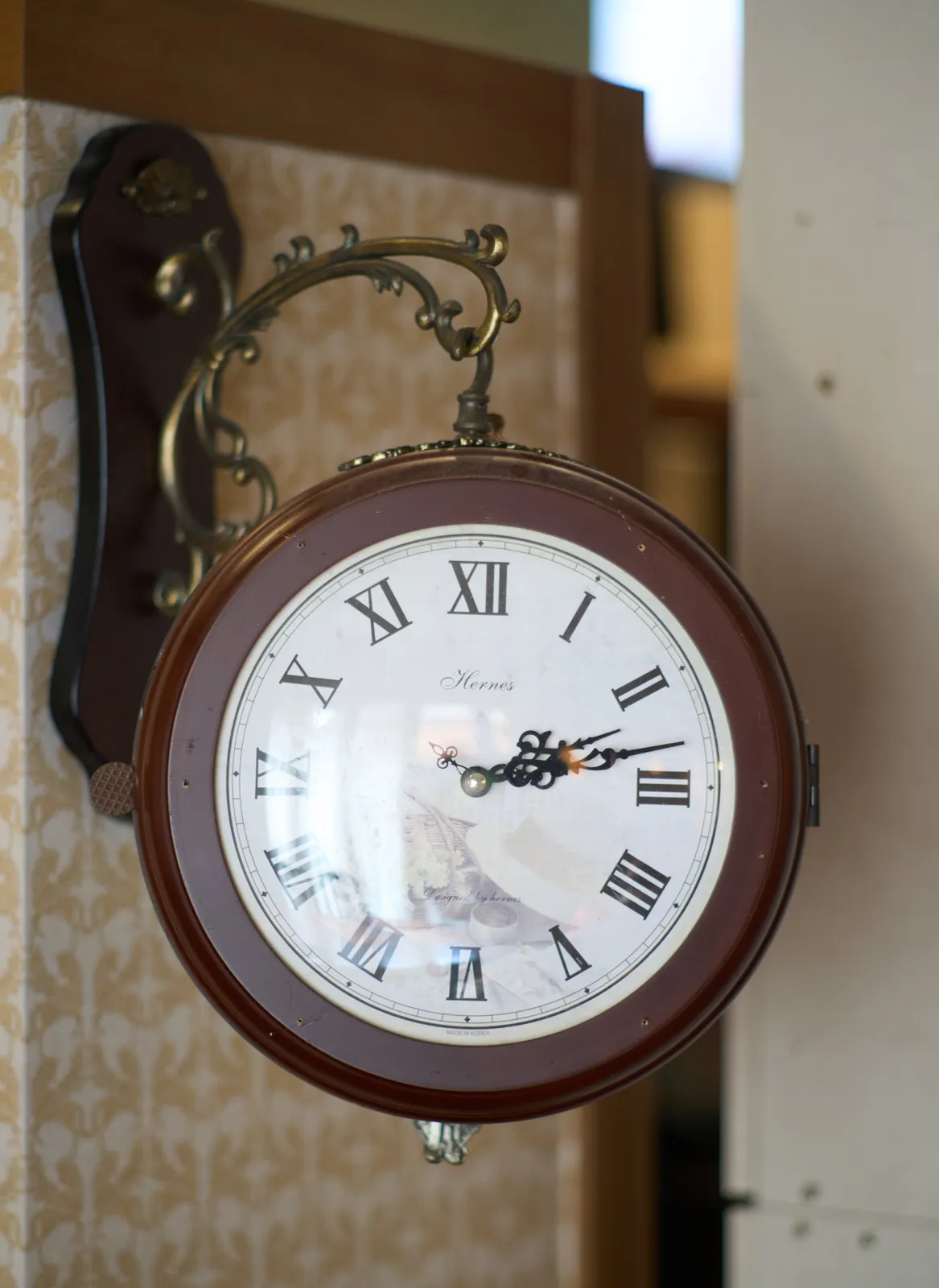 A clock hanging from an ornamental hook. It points at 13 minutes past 2.