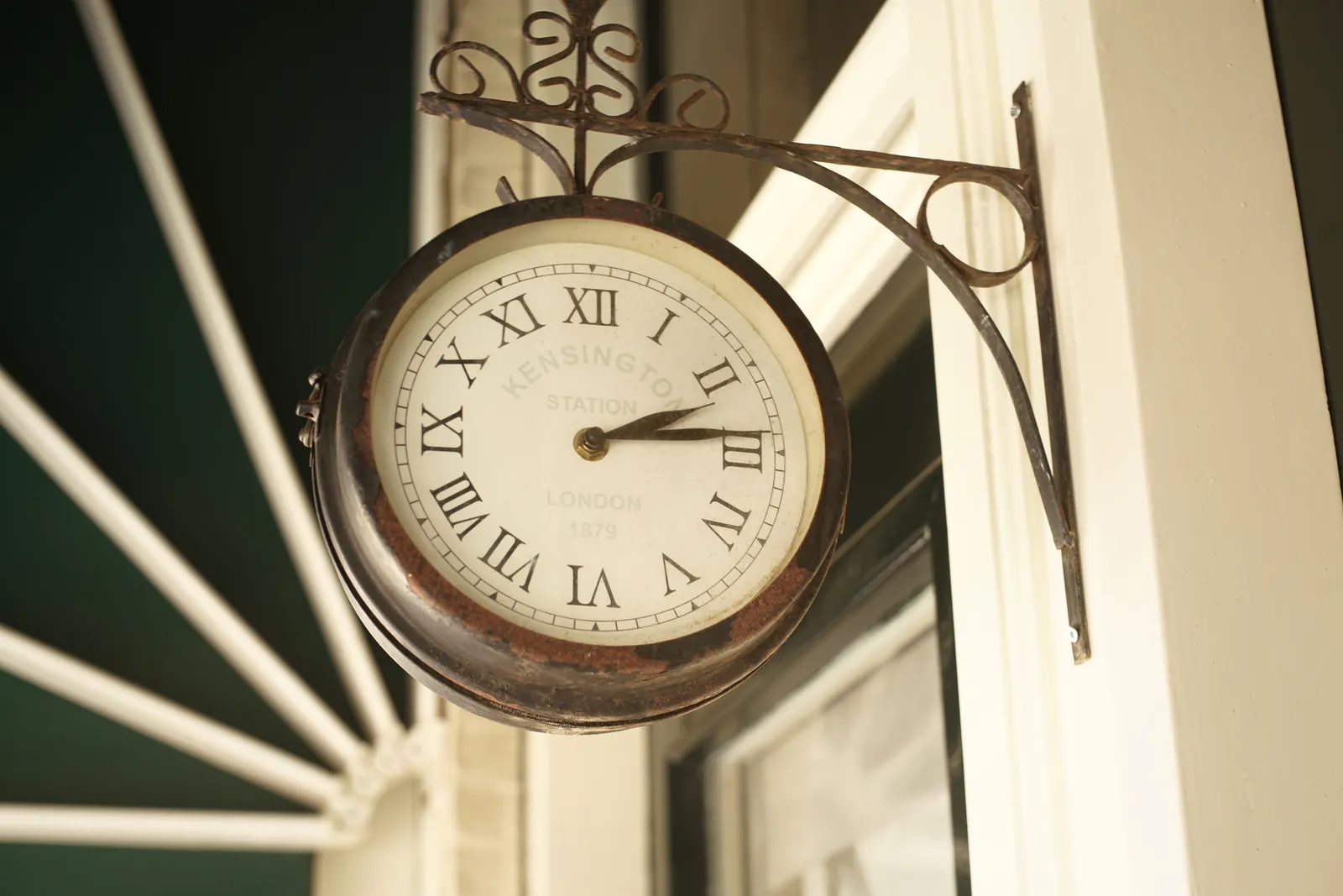 A clock attached to a building, next to a window. On it it says Kensington Station London 1879, which is not true, this picture was taken in Leiden in the Netherlands. The clock points at 14 minutes past 2.