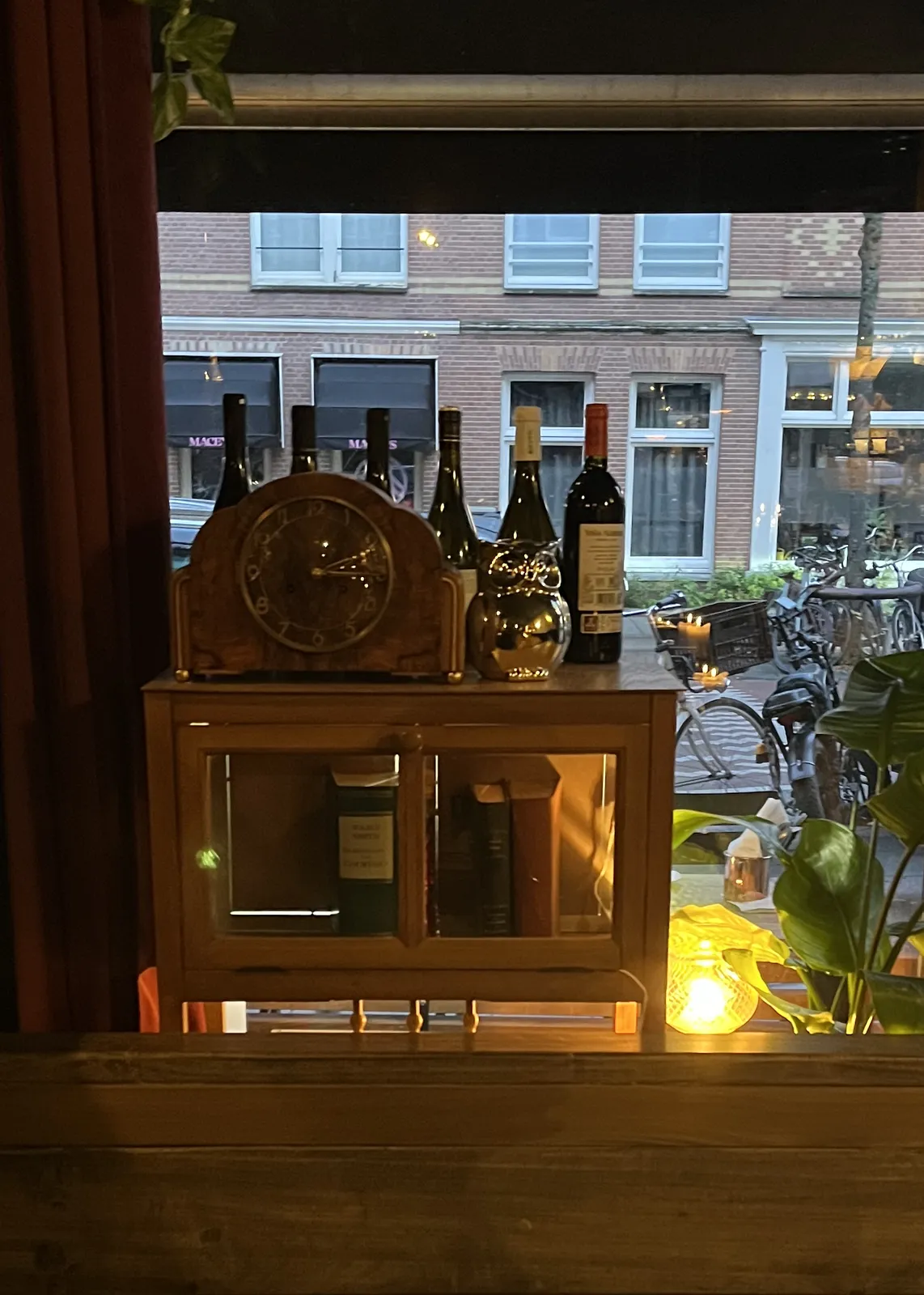 Looking out, through a window, past a cupboard with books, with an old, wooden mantel clock on top. This clock points at a quarter past two.