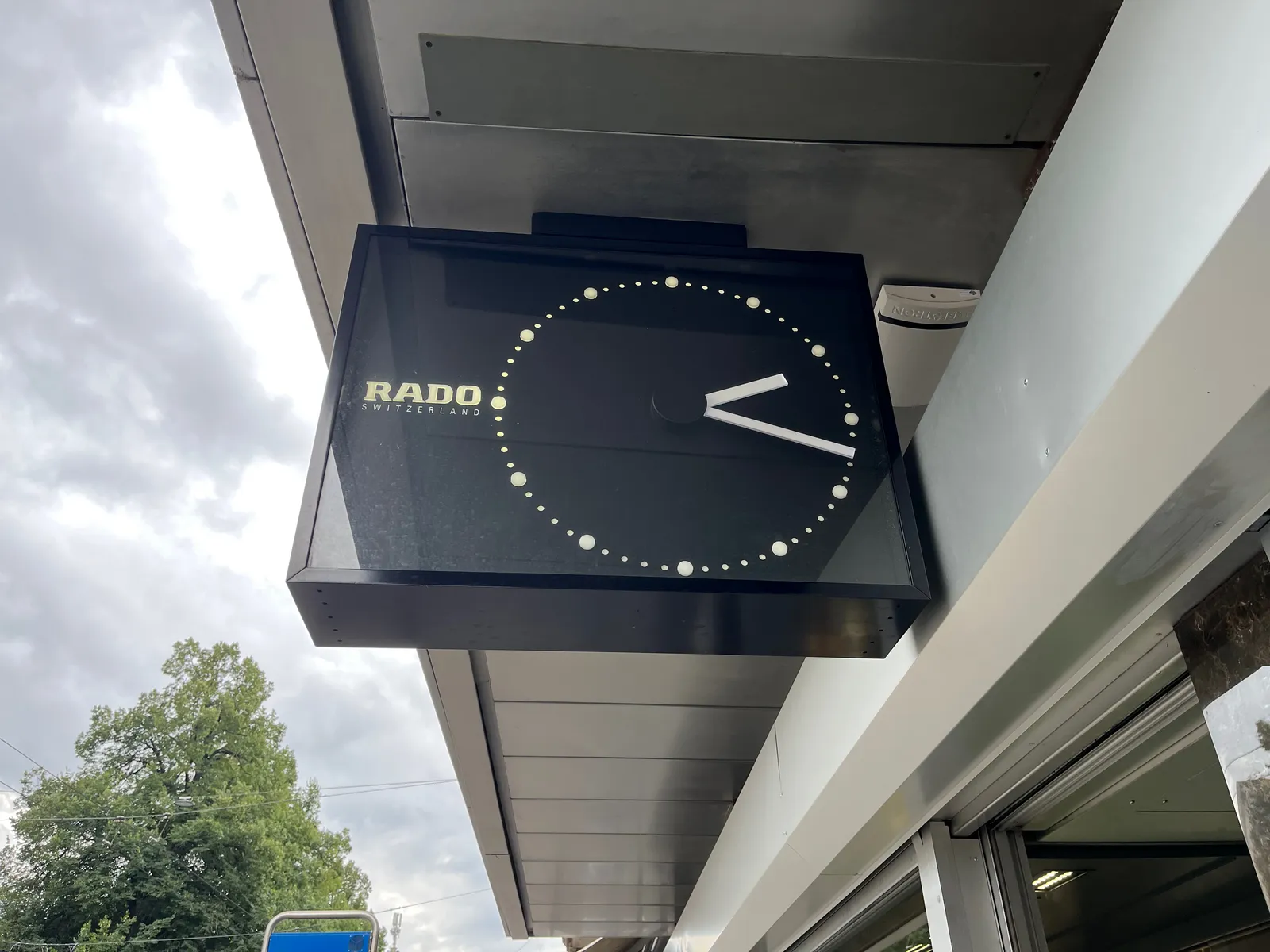 A minimalist black clock, attached to a shop. It points at 17 past 2.