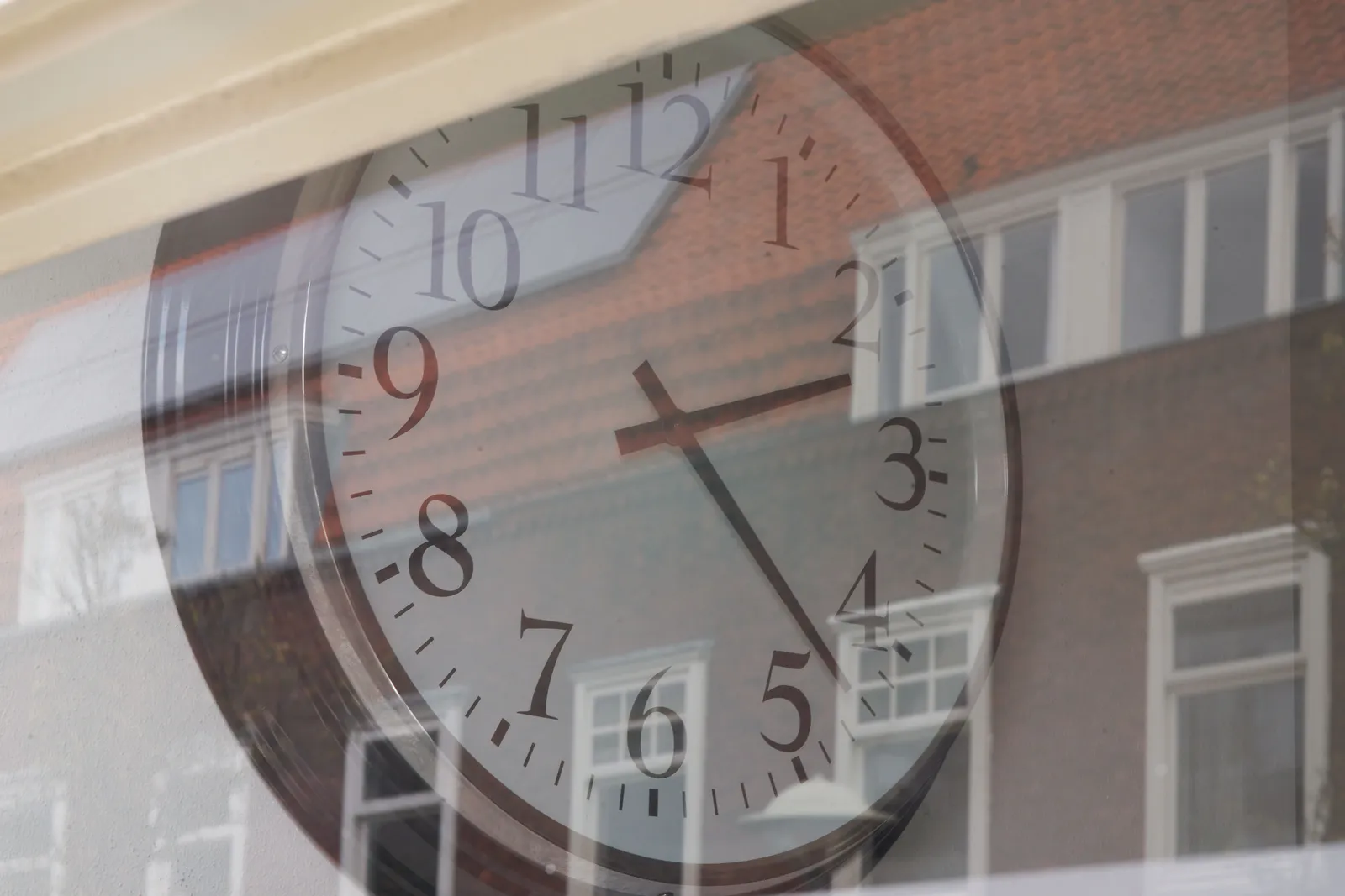 In the reflection of the window some houses can be seen. Through the window there’s a clock which point at 22 past 2.