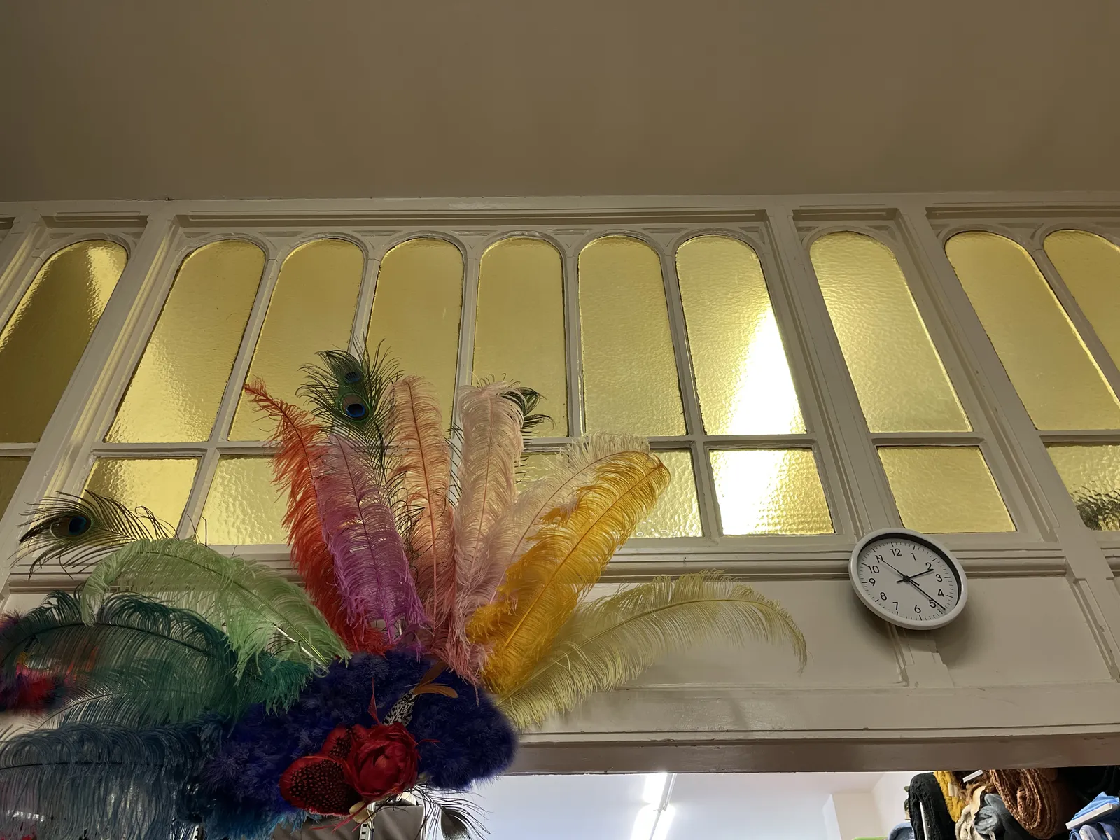 There are some very colourful, large feather on the left on this picture. There’s also a clock hanging on an elegant glass wall. This clock points at almost 24 minutes past two.