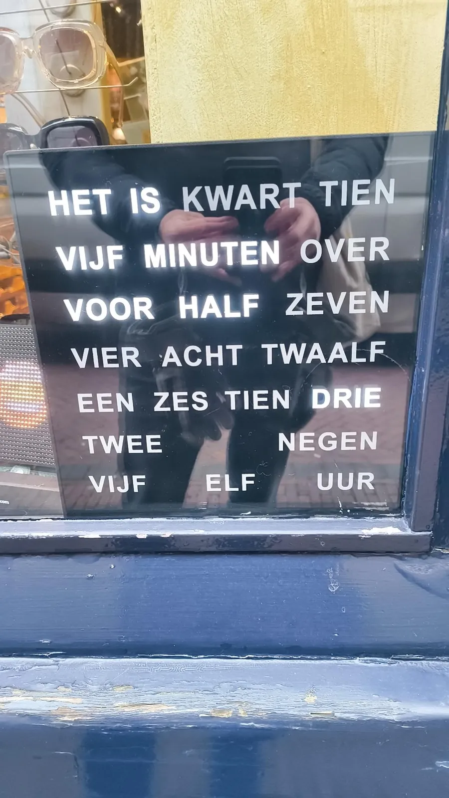 Behind a window there’s a clock made from dutch words. They are all the words you need in Dutch to be able to tell the time with a five minute precision. The words needed are highlighted, so they are a bit brighter than the other words. Right now, the combination of words is highlighted that say something like: It is five minutes before half past two, which is the Dutch way of saying that it is 25 minutes past two.