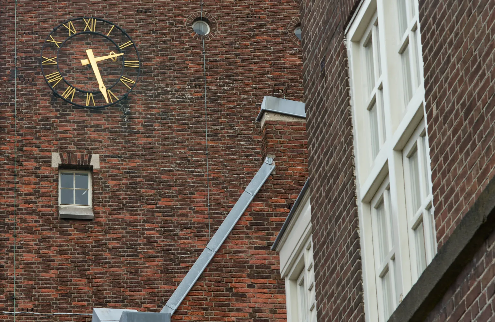On a brick wall there’s a clock with golden arms that point at 26 past 2.