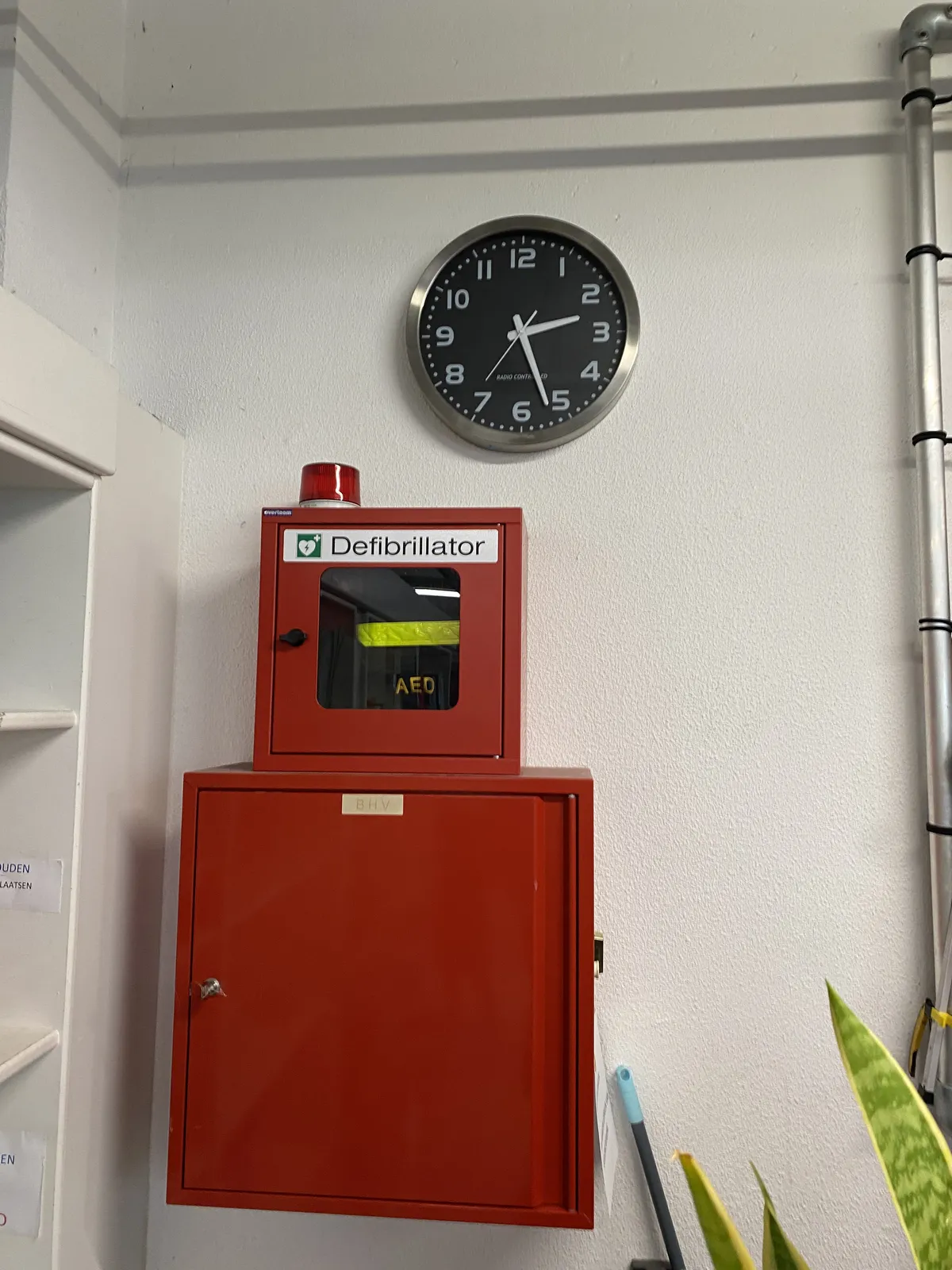 Above a defibrillator hangs a clock. It points at 27 past 2.