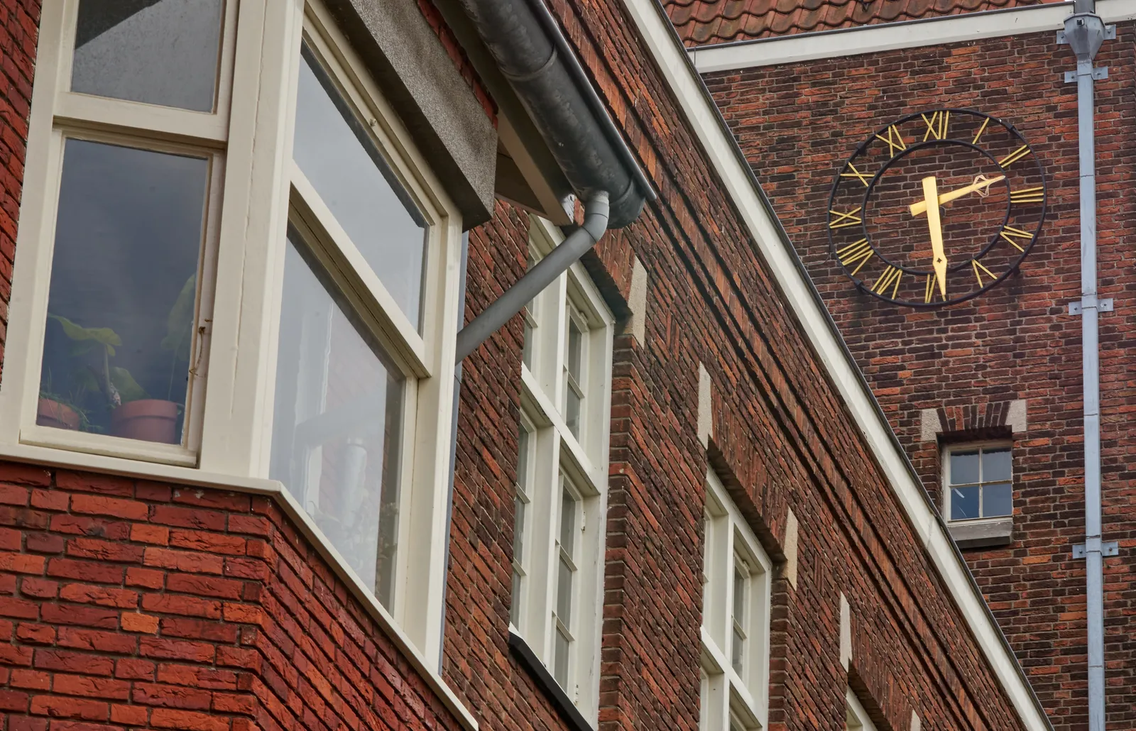 On a wall of a building built with bricks there’s a clock with golden arms that points at 29 past 2.