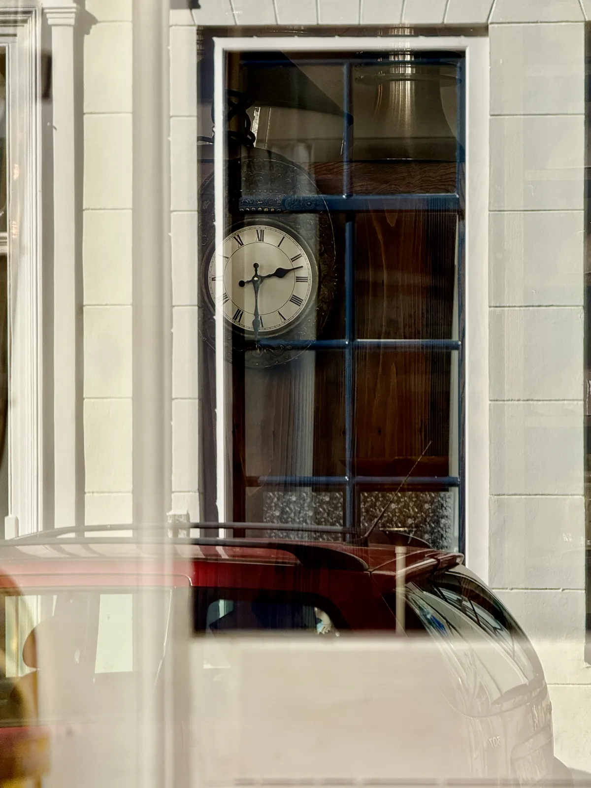 Looking out from a window, maybe from a bus, at an antique clock behind a shopping window. It points at half past two.