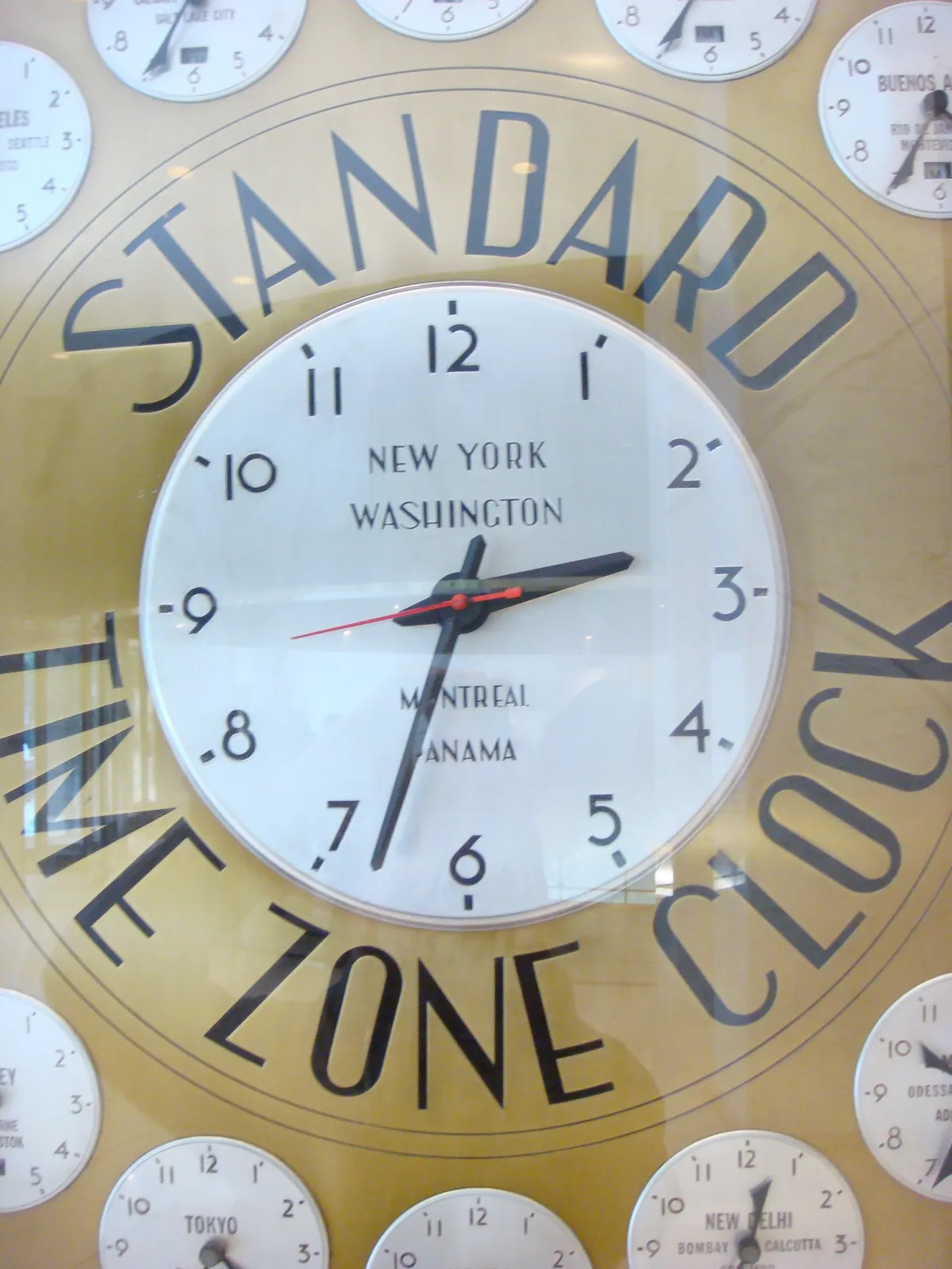 A standard time zone clock, according to the wording on its face. On all hours there’s a small clock that shows the time in a certain city in the world. The picture is framed in such a way that on none of these little clocks you can see what time it is. Only on the center clock, which shows the time in New York, you can see that it is 33 minutes past 2.