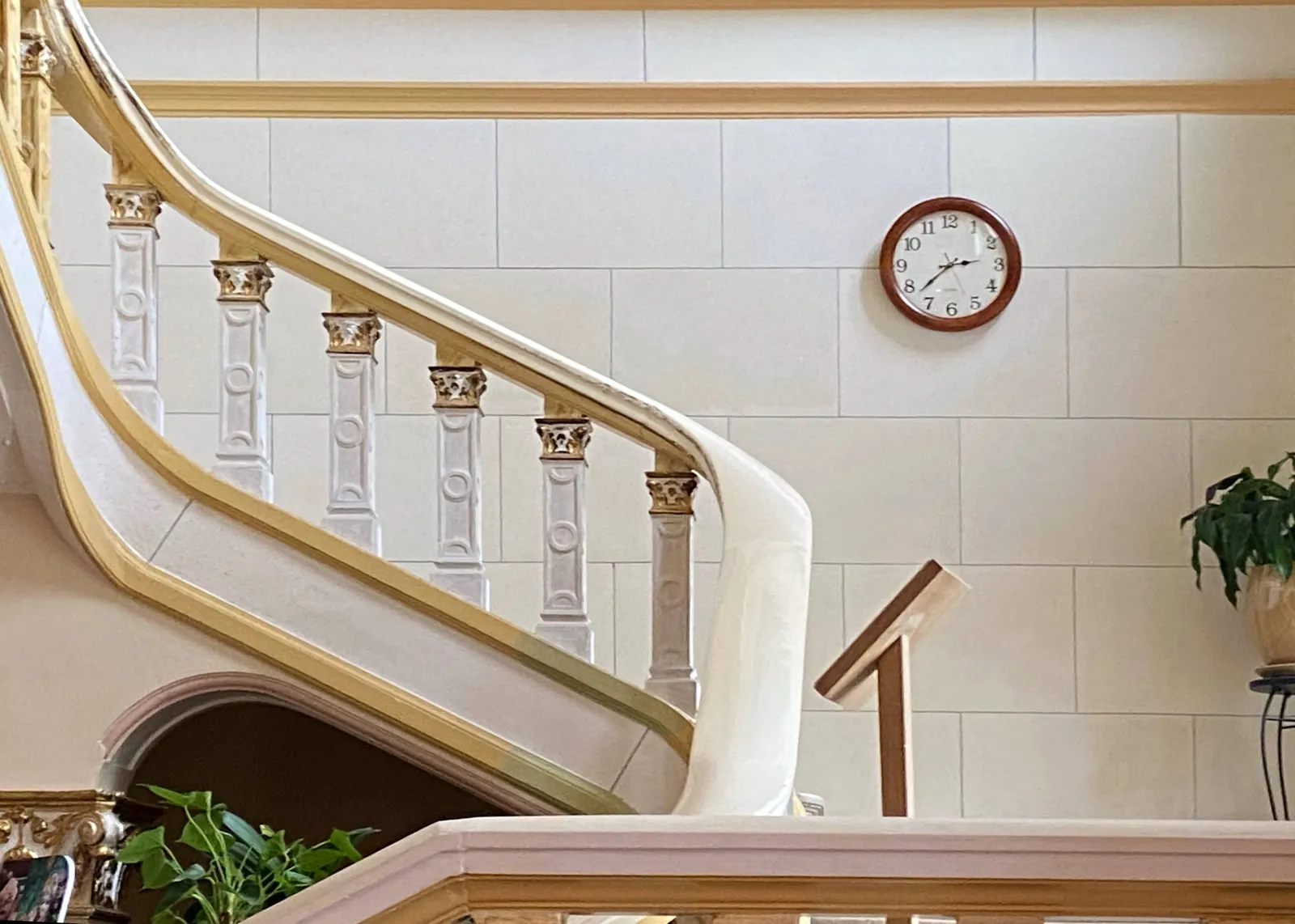 Next to some old stairs, on a white brick wall, there’s a clock. It points at 37 minutes past 2.