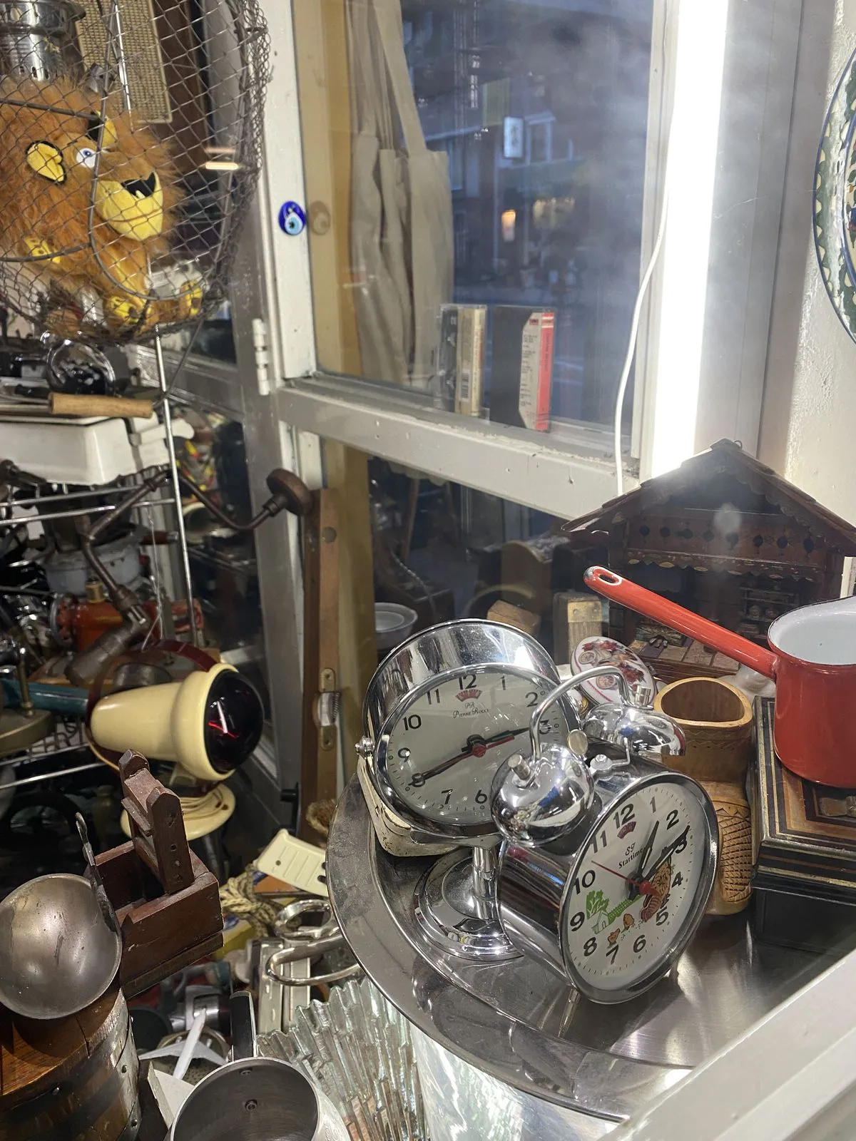 A picture of stuff in a thrift shop. There are two clocks. The one in front points at approximately 14 minutes past one, and the one in the back points at 20 minutes to three.