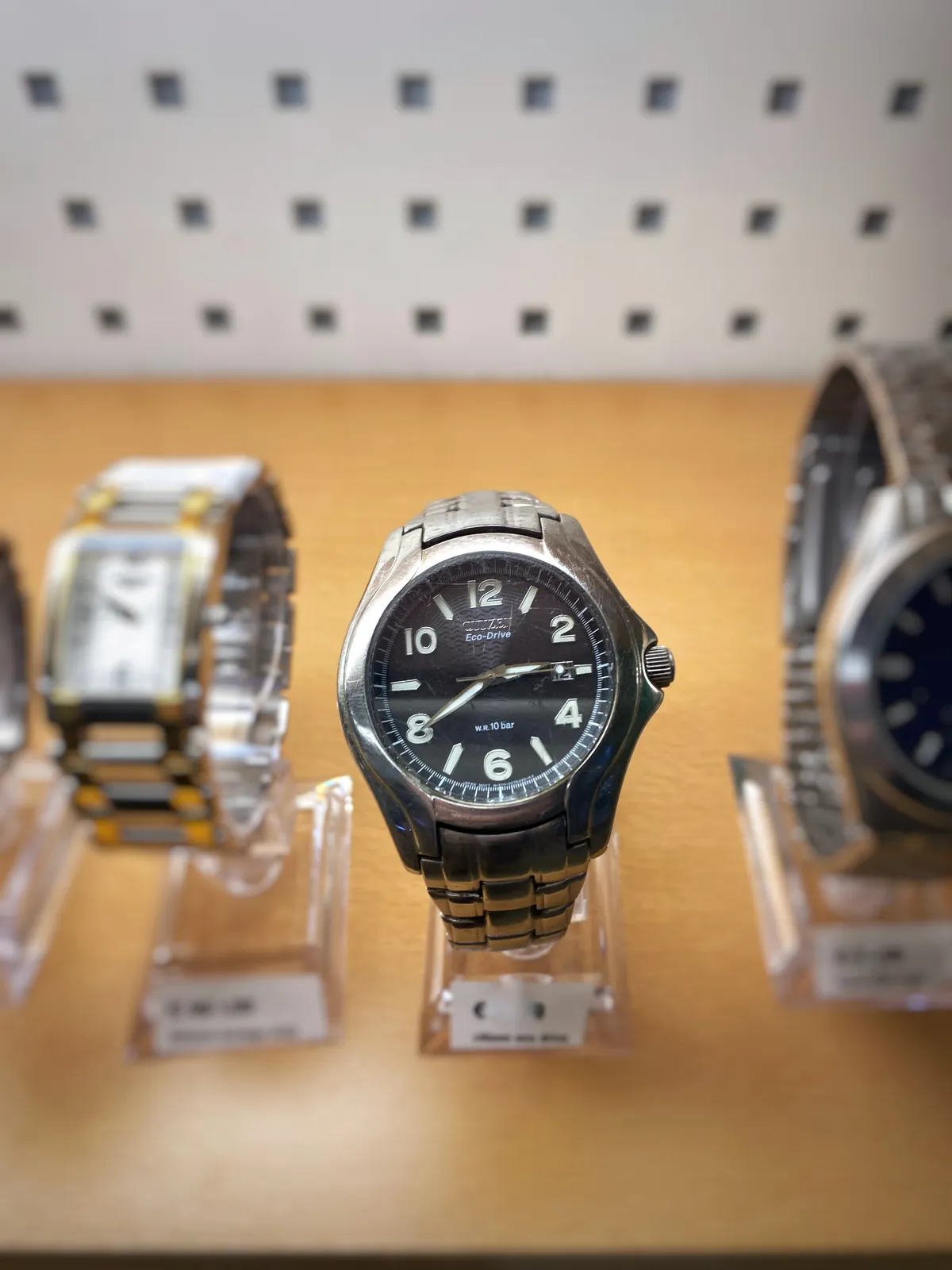 A row of watches on display. One of them is in focus. It points at 20 minutes to 3.