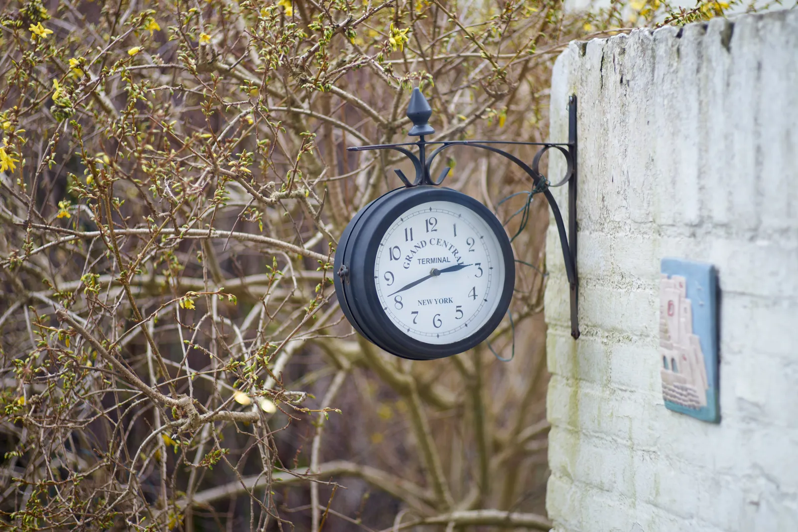 A Grand Central clock, attached to a white wall in someone’s back garden points at 41 minutes past 2. 