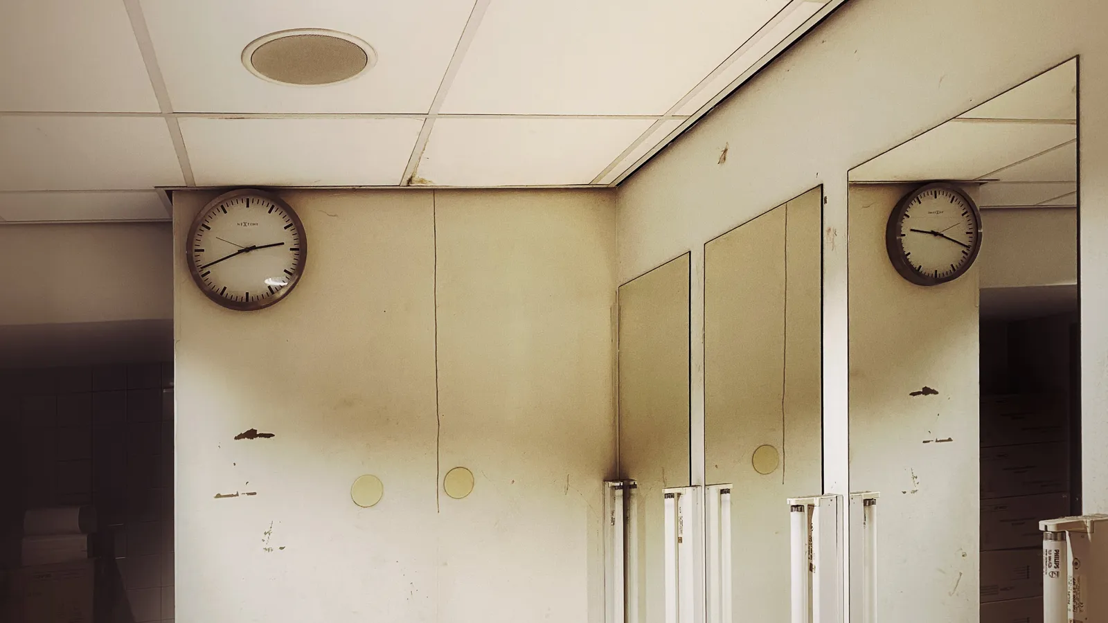A clock in an old shabby dressing room. It points at 41 minutes past 2. You can see the clock in the mirror as well. This mirrored clock points at 18 minutes past nine. 
