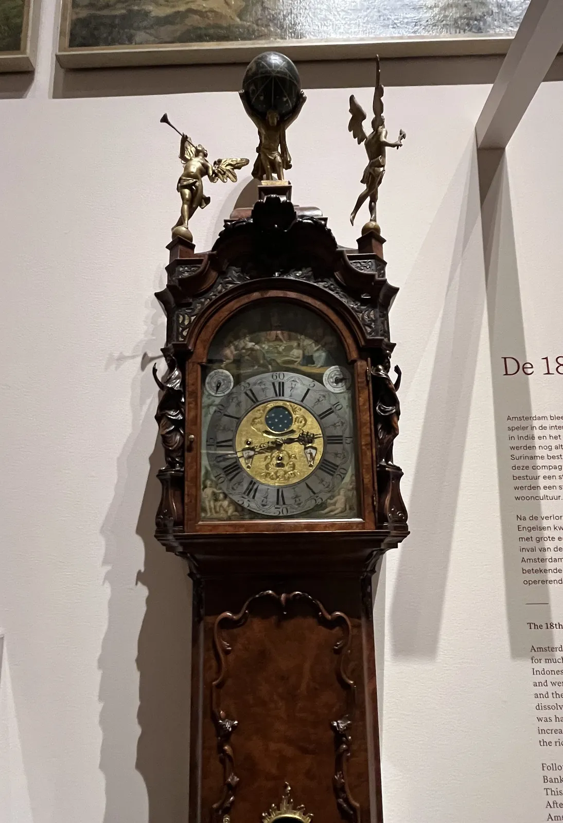 A standing clock with many fine details. The clock points at 17 minutes to 3.