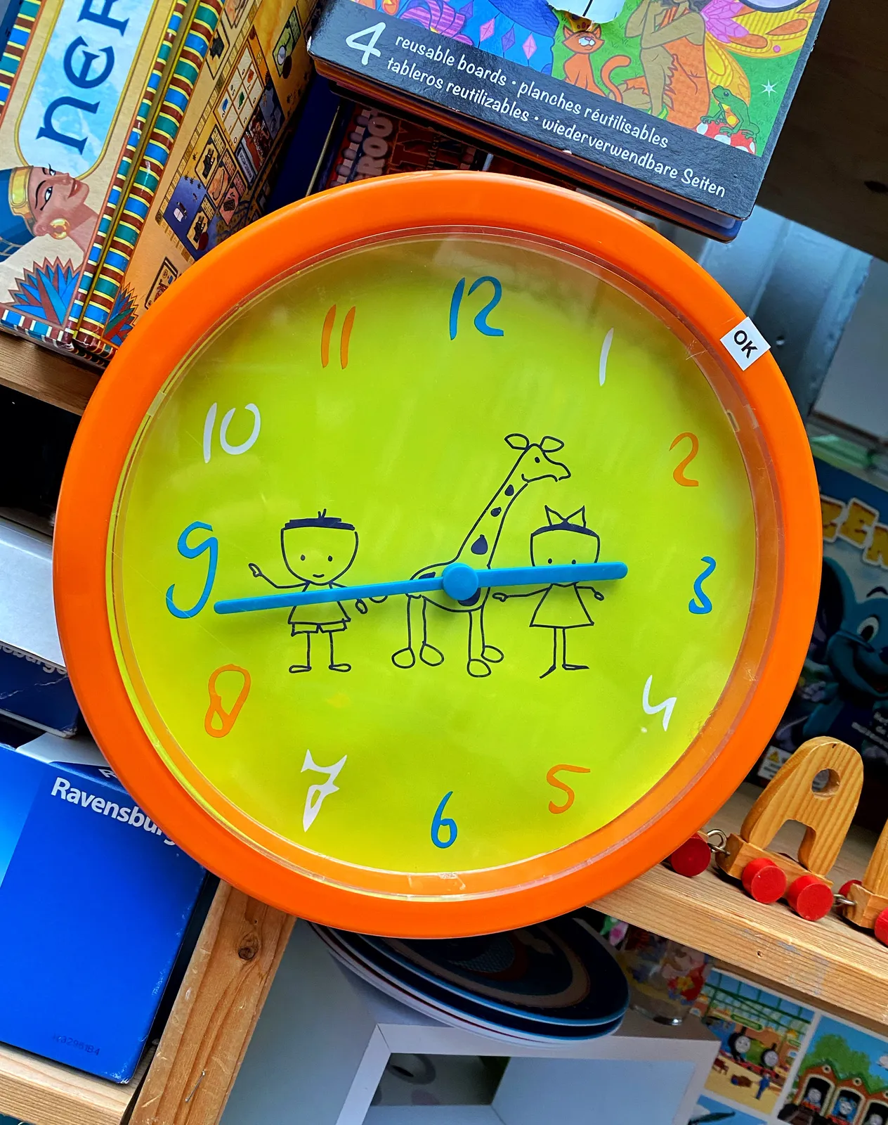 A colourful clock with two kids and a giraffe drawn on its face. It points at 43 minutes past 2.
