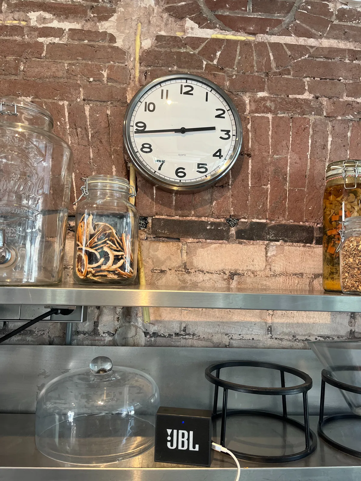 Some things in glass jars. The jars stand in front of an old brick wall. On this wall there’s a clock that points at 17 minutes to 3.