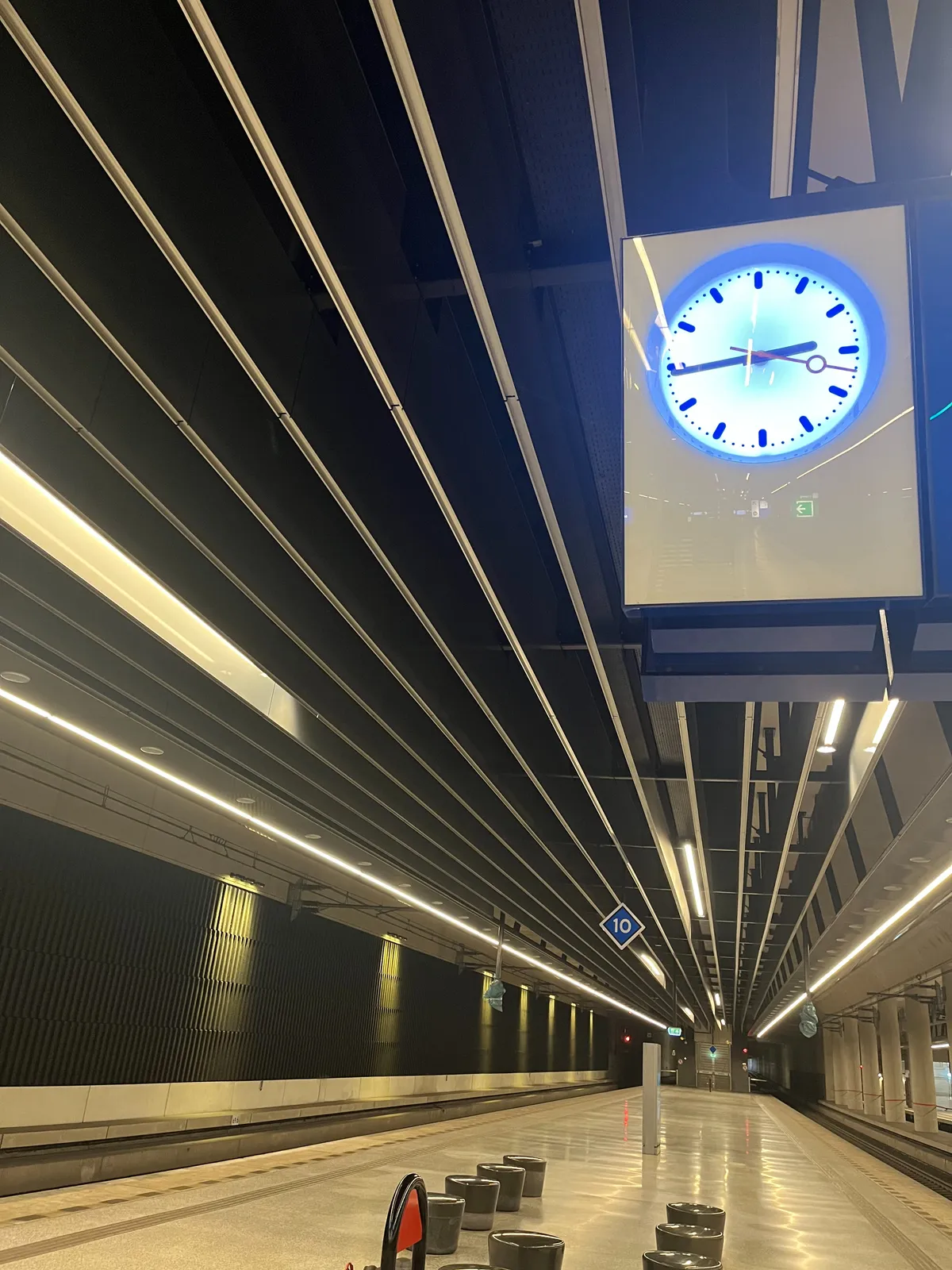 A clock in a rather modern, clean and shiny train station. It points at 16 minutes to three.