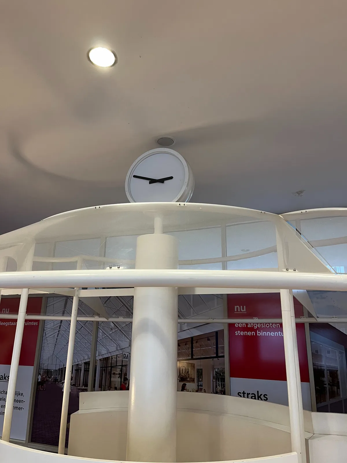 A minimalist clock, placed on a white structure with an unclear function. The clock points at approximately 13 minutes to 3.
