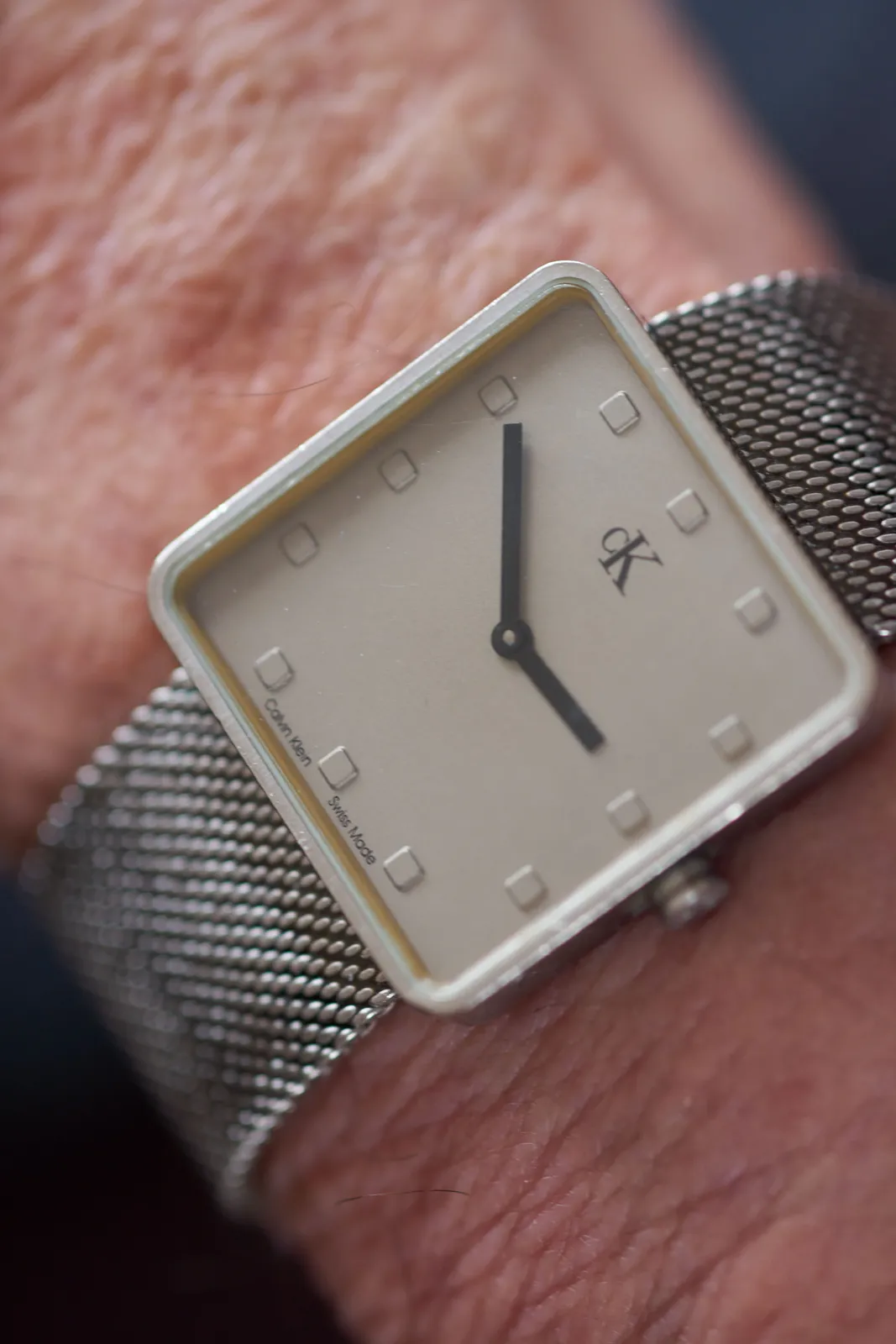 This square, minimalist wrist watch, on someone’s wrist, points at 10 to three.