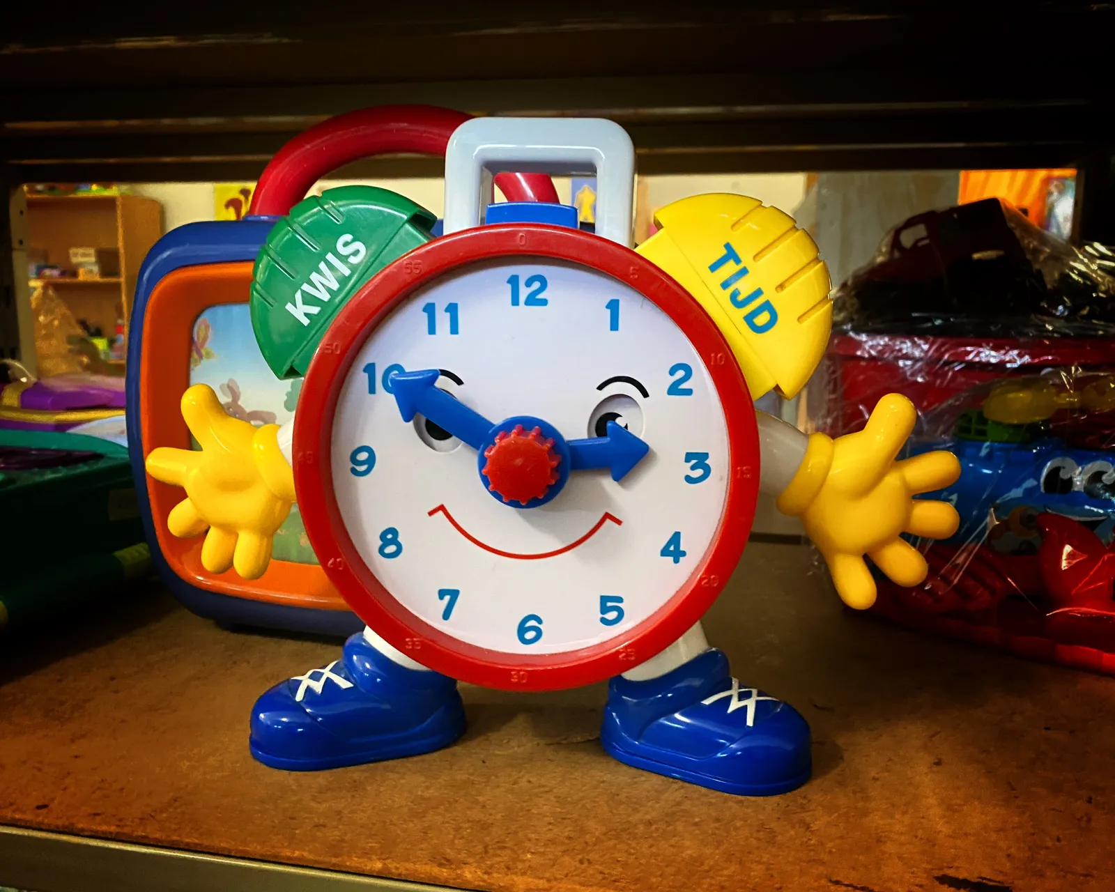 A very colourful toy clock, with a face and hands, points at ten minutes to three.