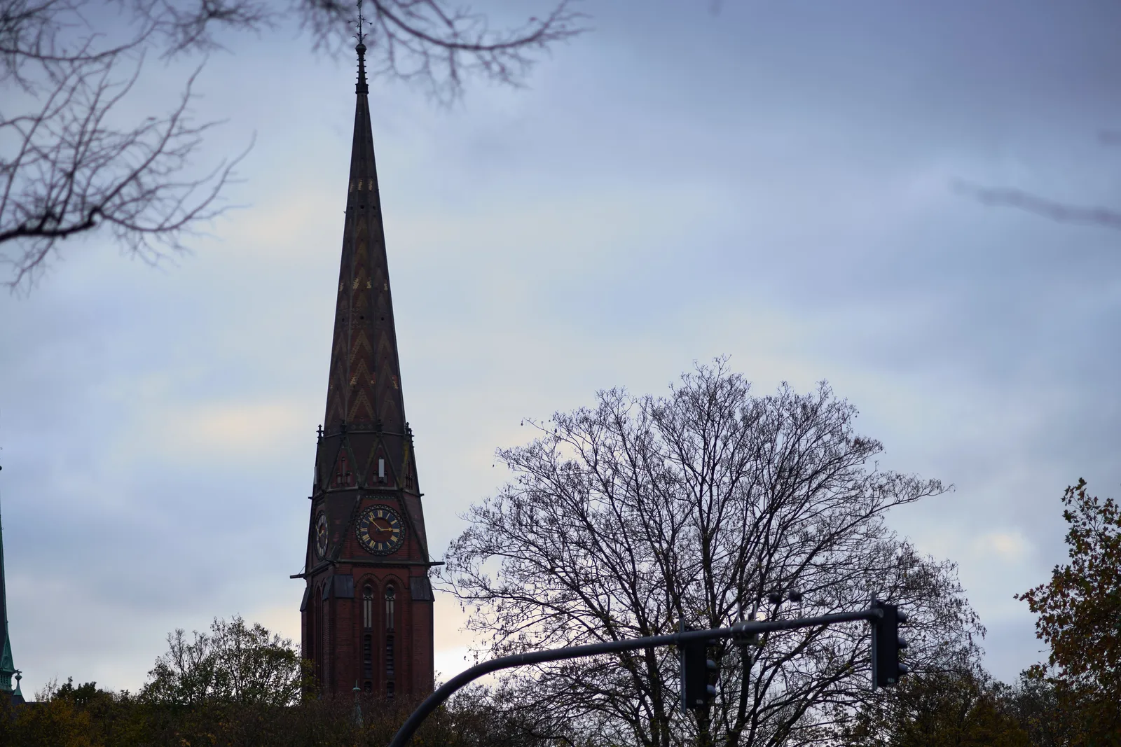 Some silhouettes of trees without leaves on a grey sky. There’s also a large, rather thin church tower with a clock which points at 8 minutes to 3.