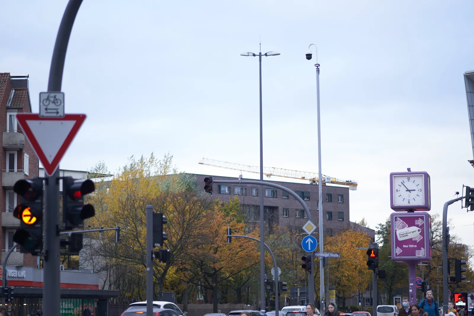 A general cityscape with some buildings, a traffic light and a clock. It is 7 minutes to 3.