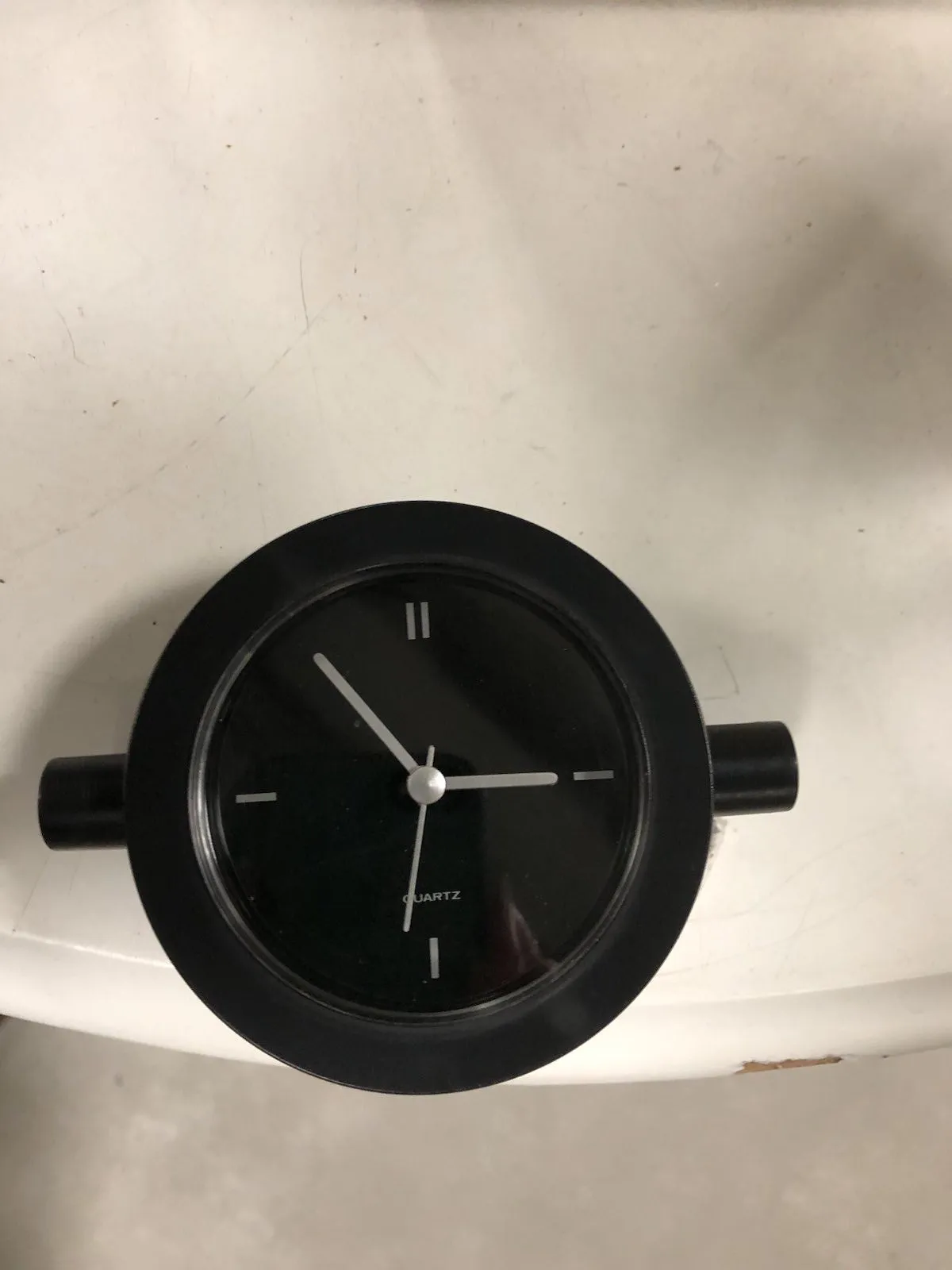 A black clock on a white background seems to point at approximately 7 minutes to three.