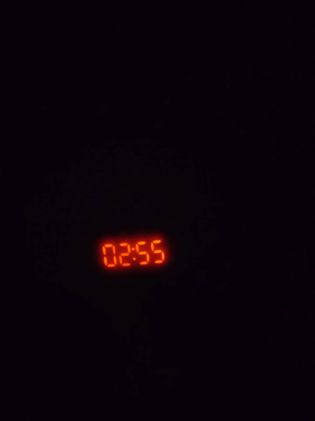 An almost completely black picture with in the middle a digital clock, with red digits. It says it is 02:55