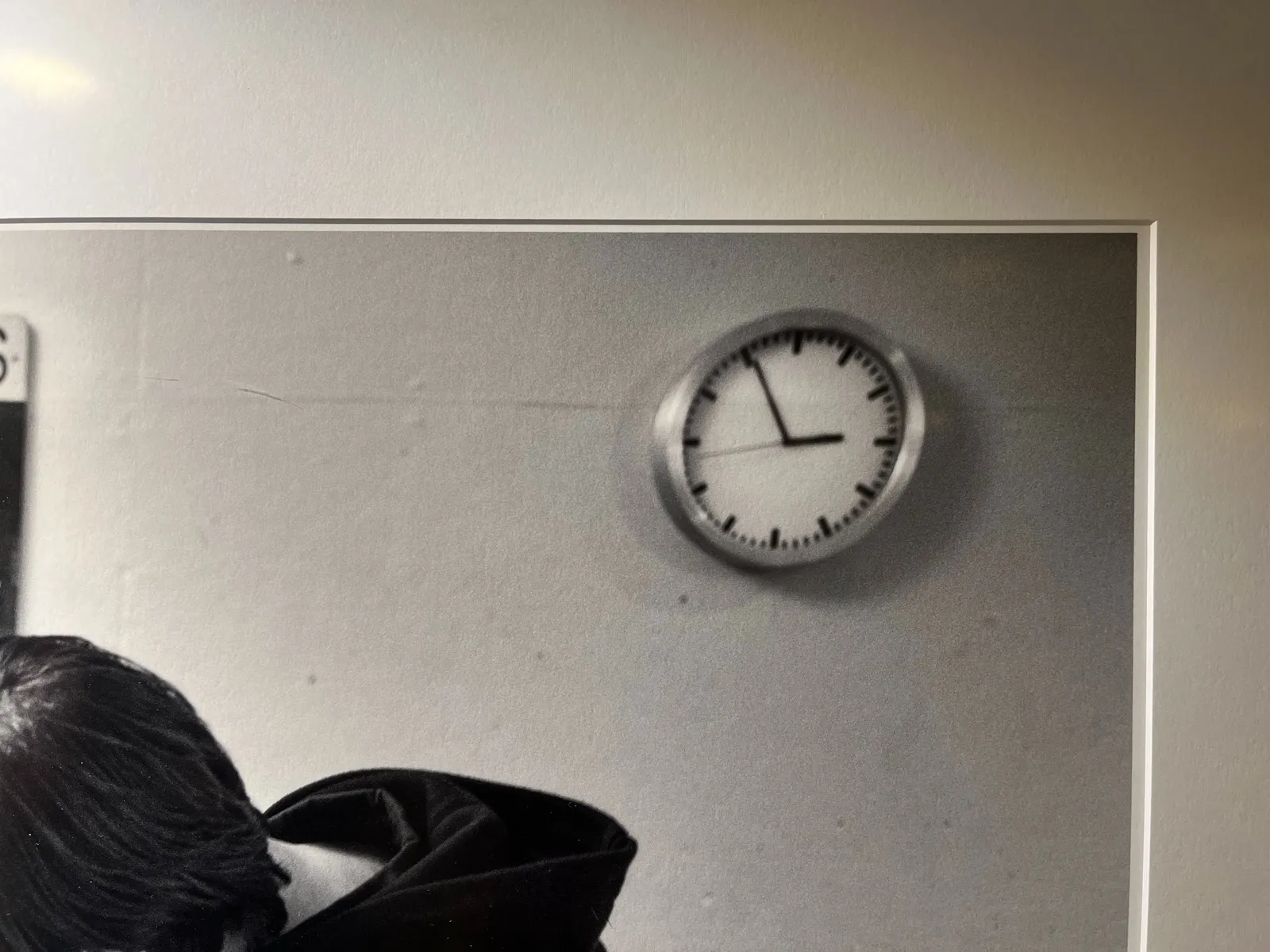 A picture of to the top right corner of a framed photograph where you can see a clock. The clock points at 5 minutes to 3.