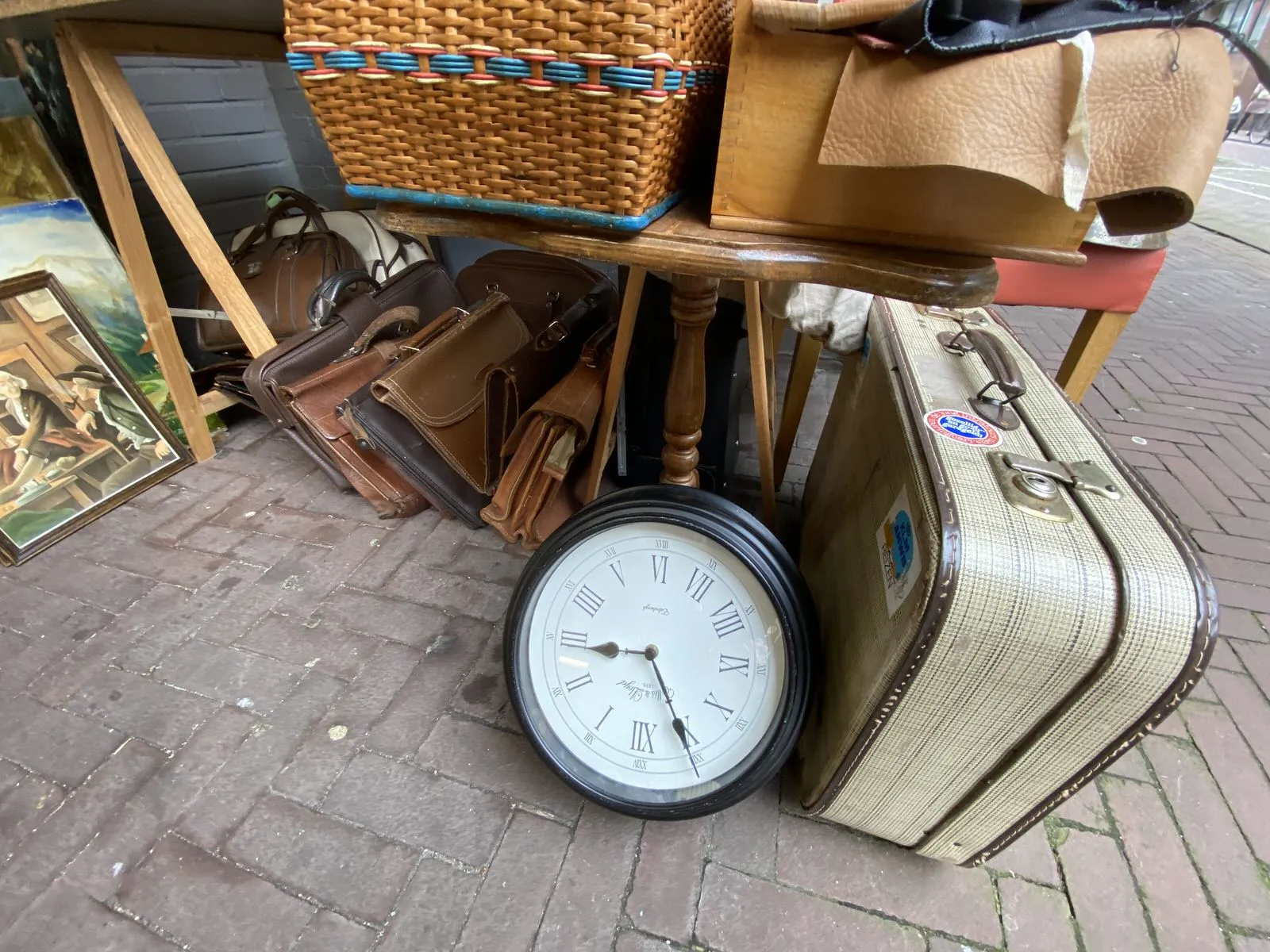 A clock in a thrift shop stands upside down between some things like old suitcases. It points at four minutes to three.
